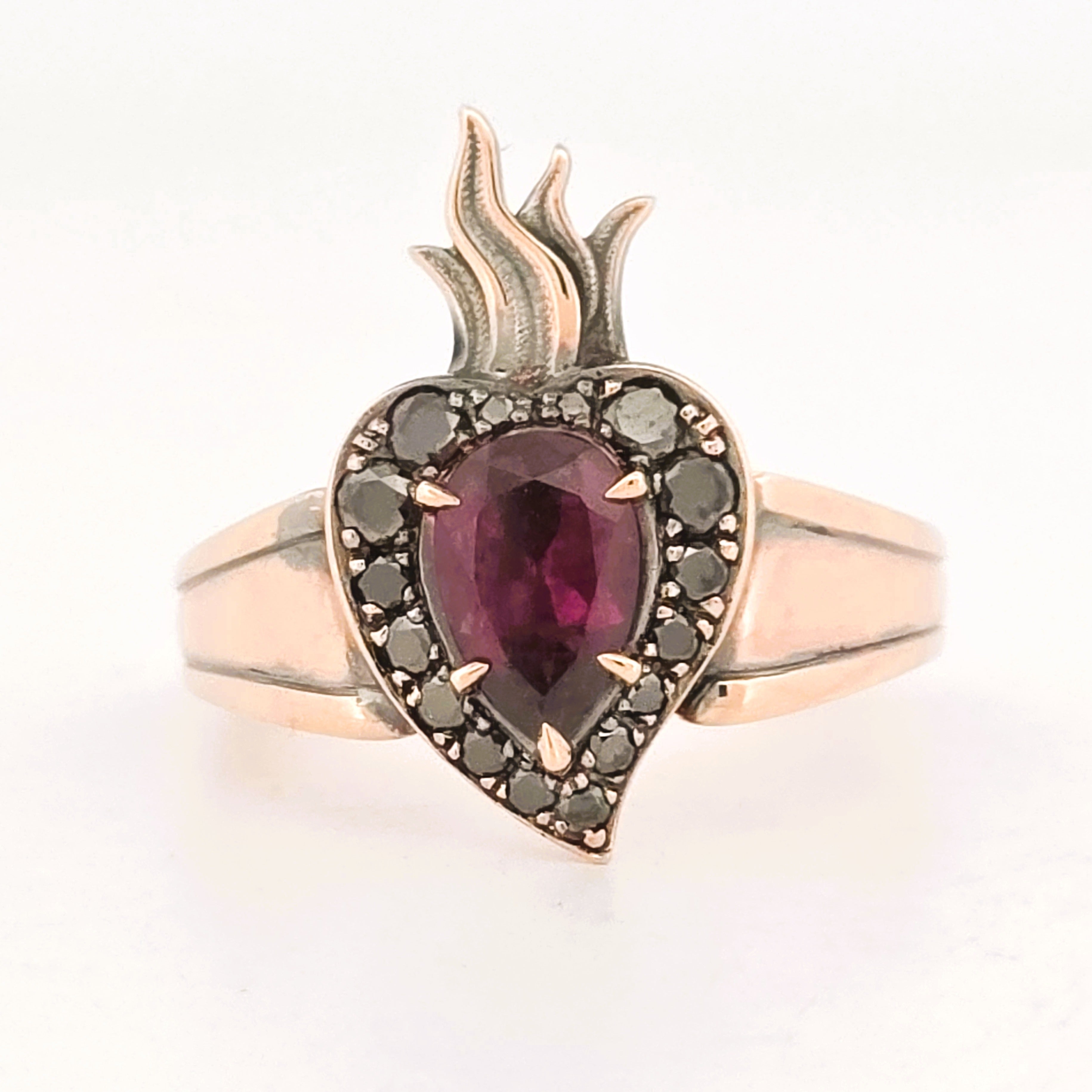 Rose gold flaming heart ring featuring a pear-shaped garnet surrounded by black diamonds.