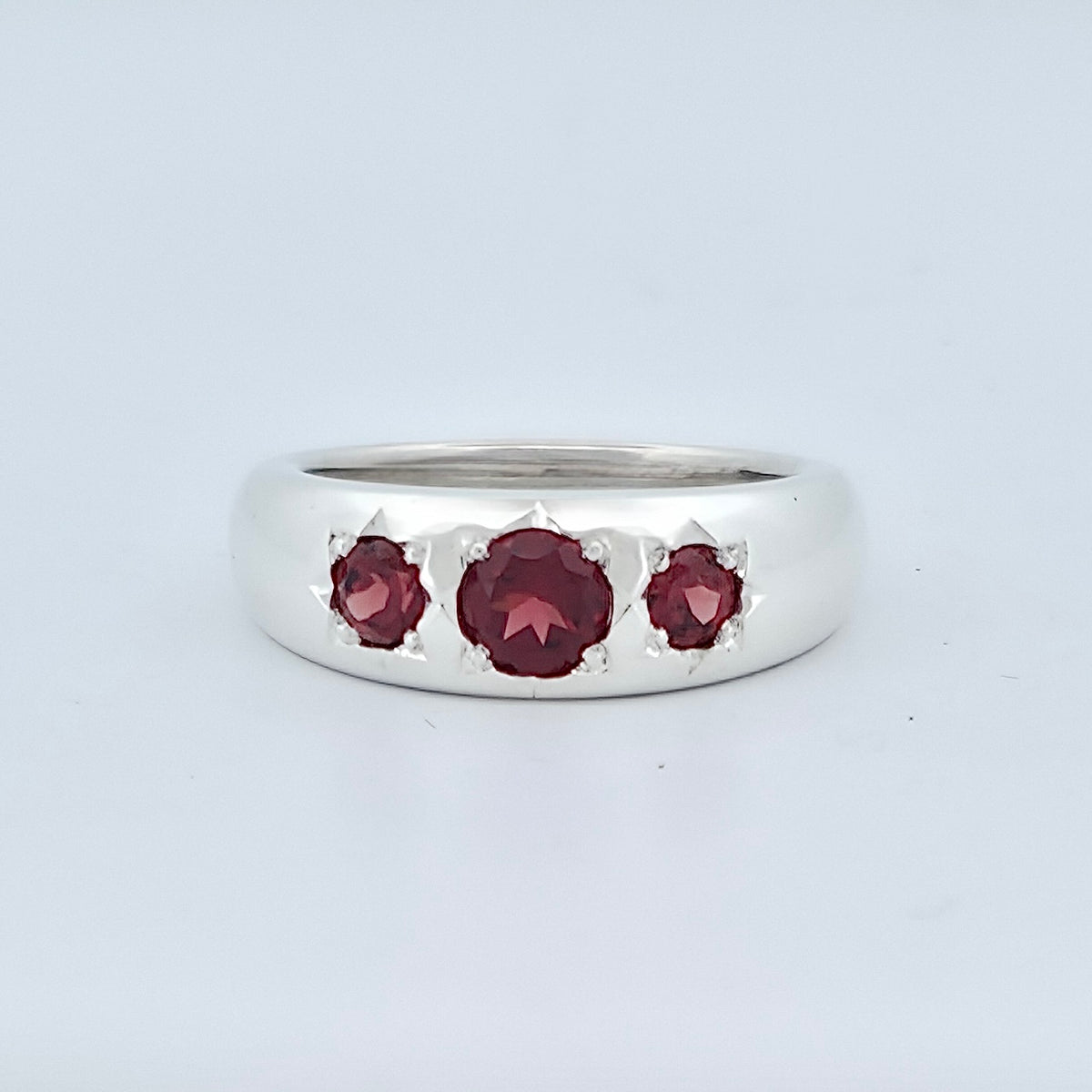 Front facing polished silver statement ring featuring three round, deep-red garnets in hand-finished settings, with a larger centre stone flanked by two smaller stones.