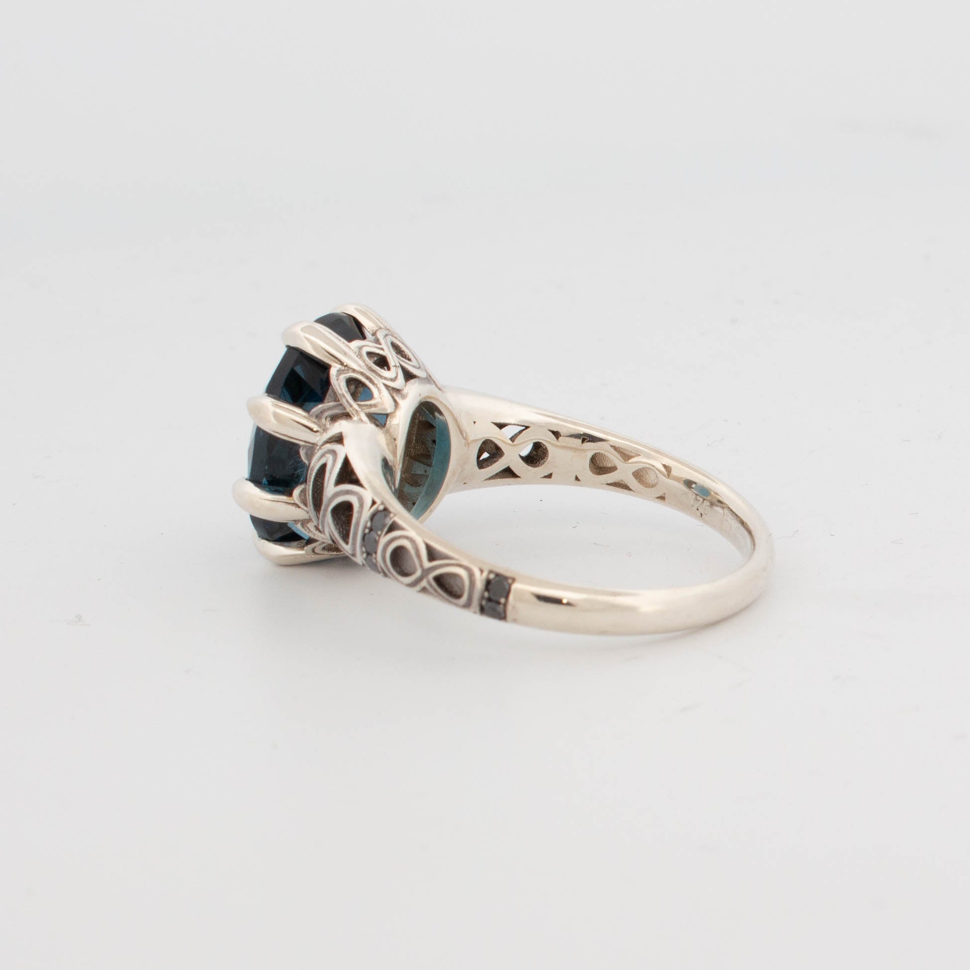 9ct white gold ring featuring a large oval-cut London Blue Topaz in a claw setting, with infinity symbol openwork shoulders and pavé-set black diamonds on the band.