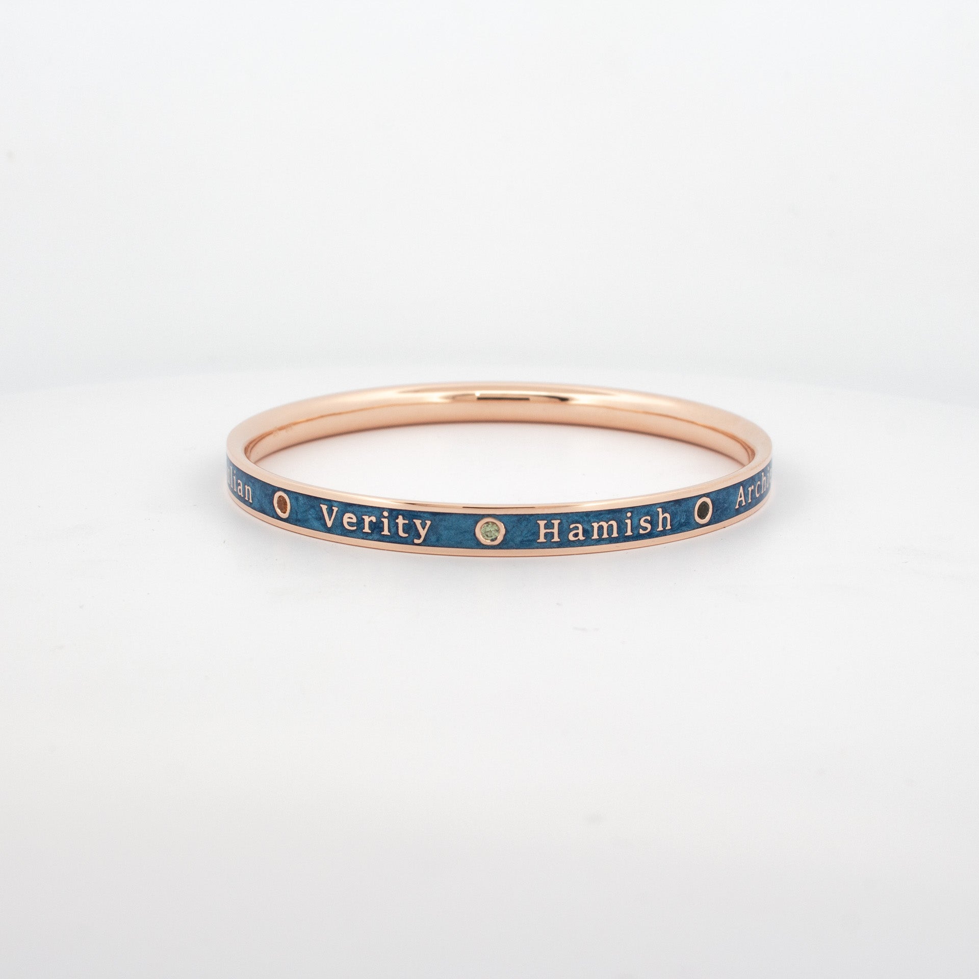 Custom rose gold bangle with blue enamel inlay, engraved names and bezel-set rubies.