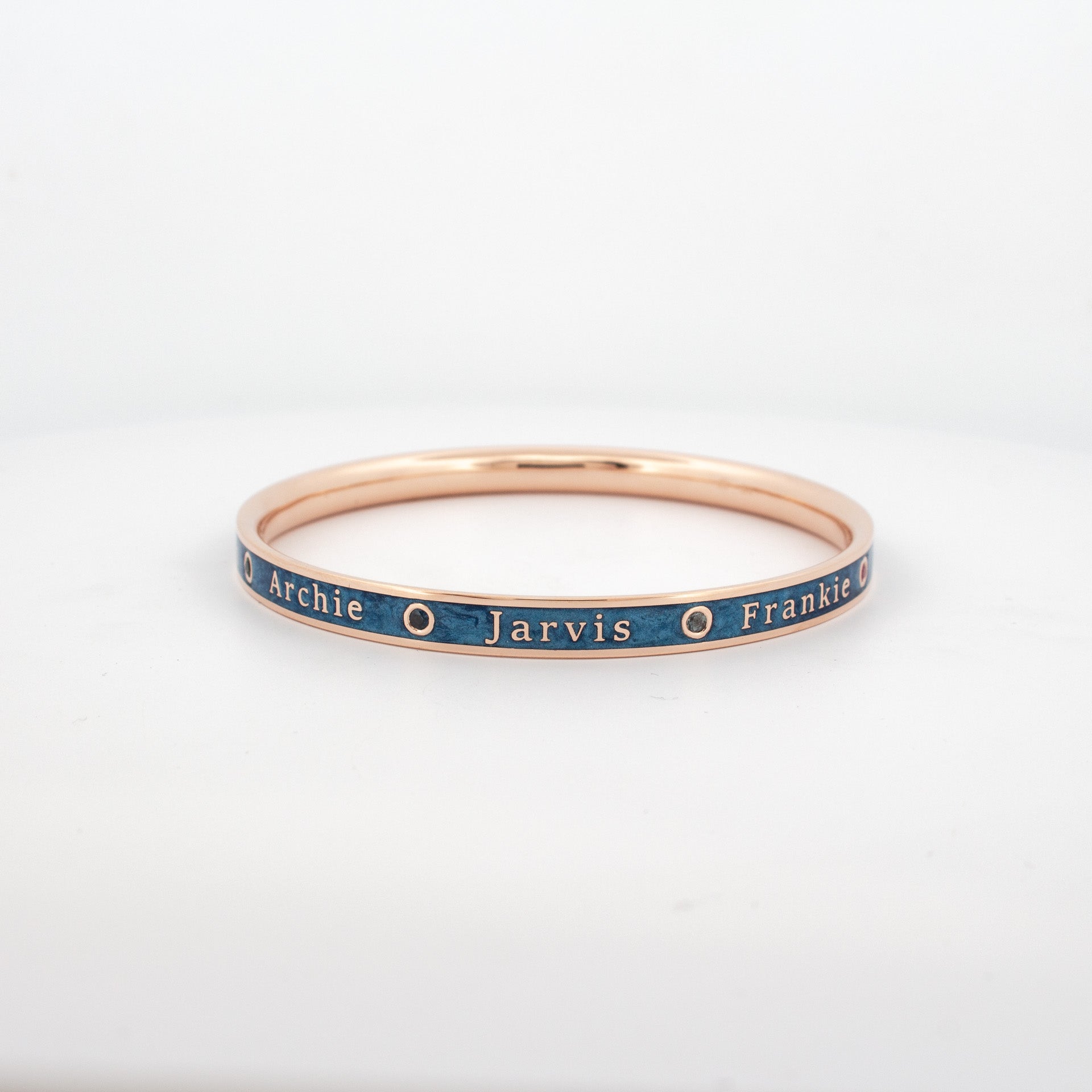 Custom rose gold bangle with blue enamel inlay, engraved names and bezel-set rubies.