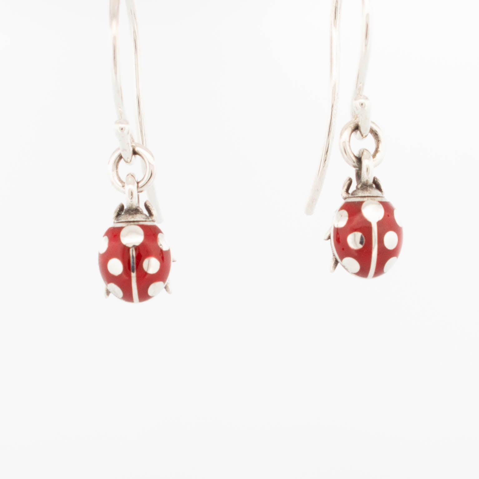 Pair of sterling silver drop earrings featuring 3D ladybird charms with glossy red enamel, suspended from curved hook ear wires; handcrafted insect-themed jewellery ideal for whimsical and nature-inspired collections.