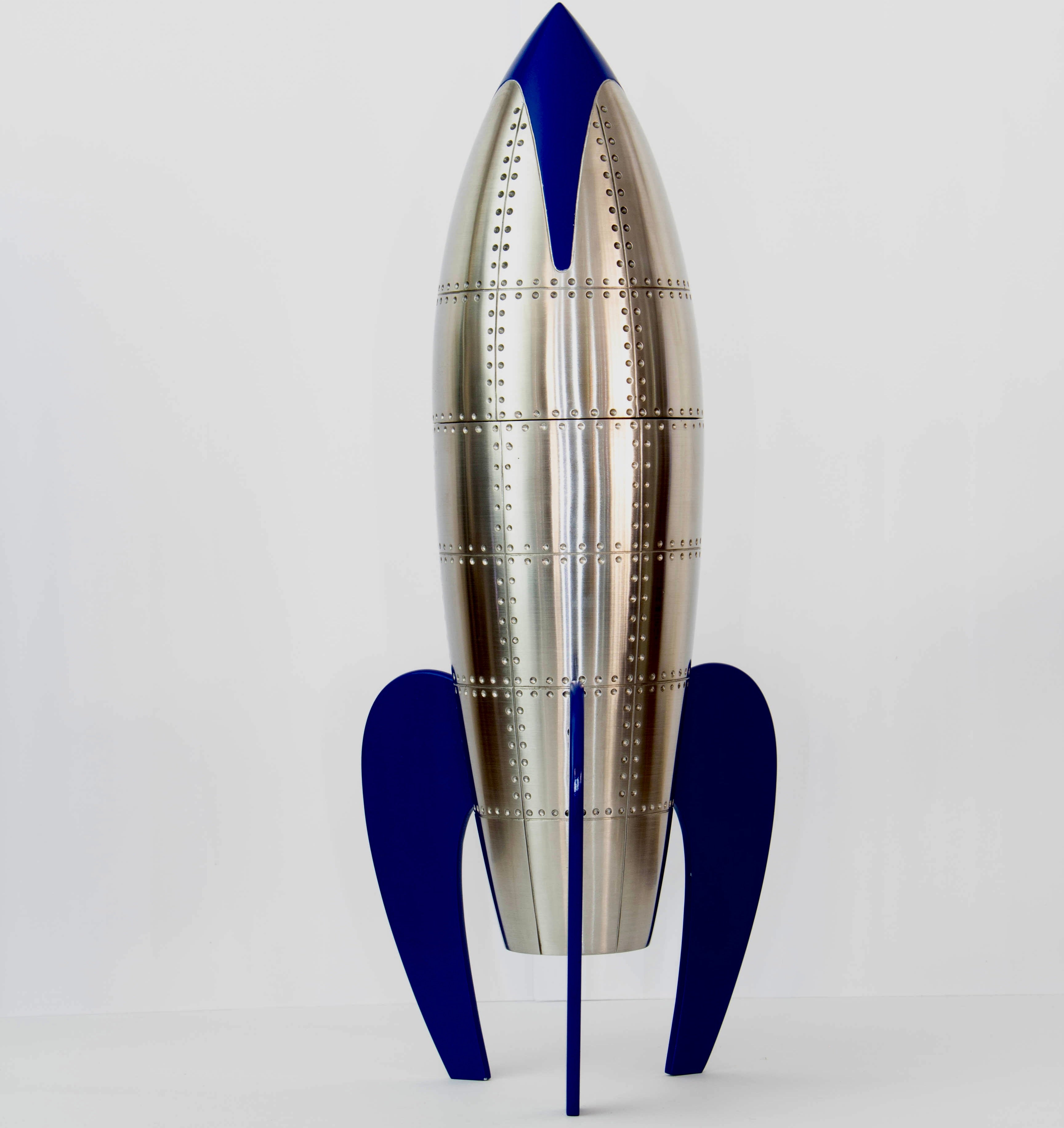 Custom cremation urn designed in the form of a retro rocket, crafted from stainless steel and brass with rivet detailing, and finished with glossy blue enamel fins and nose cone; stands 34cm tall.