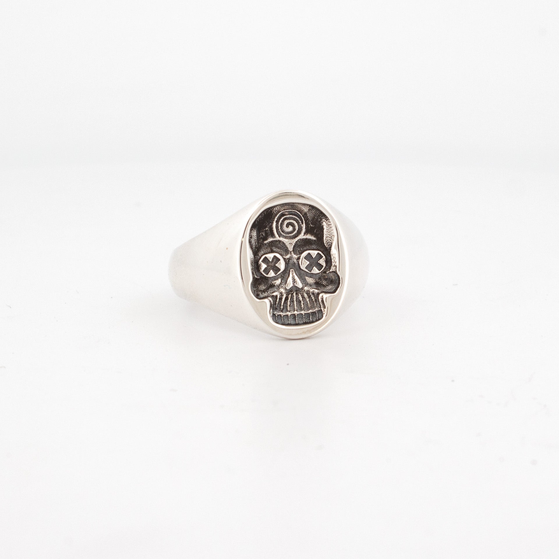Sterling silver signet ring with engraved cartoon-style skull featuring spiral forehead and X eyes.