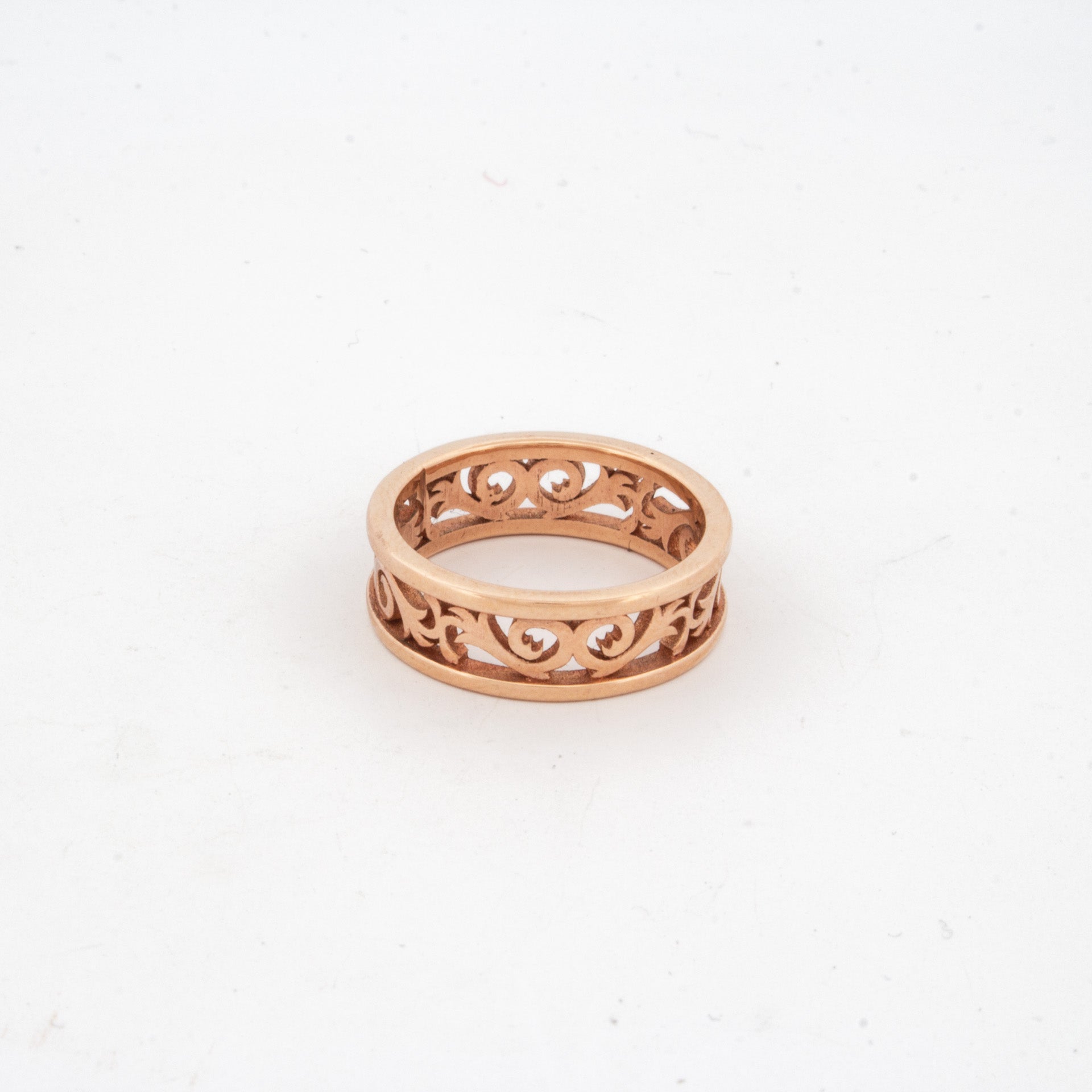 Openwork filigree ring in rose gold with scrolling vine motif and polished outer bands.