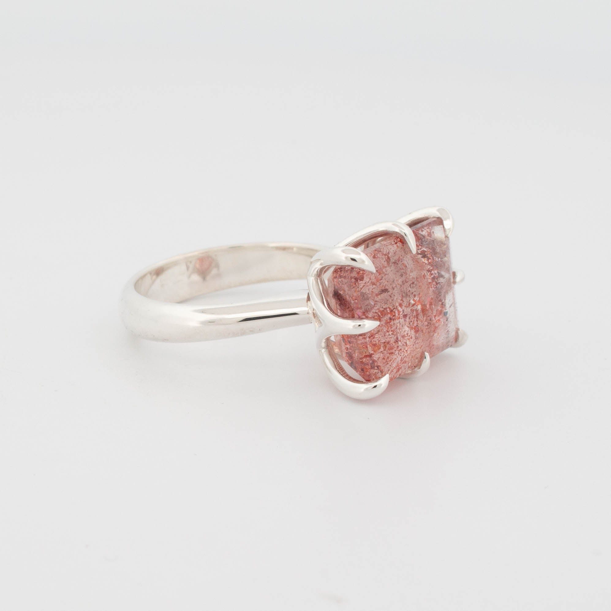 angled view of "Sterling silver ring featuring a large rectangular cabochon with a red and copper-toned splatter effect, secured by bold claw prongs; contemporary statement design known as the Splatter Ring."