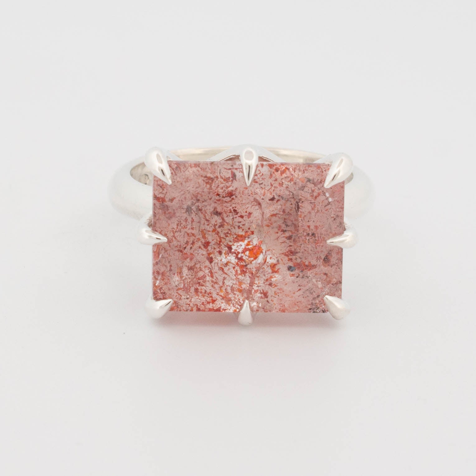 "Sterling silver ring featuring a large rectangular cabochon with a red and copper-toned splatter effect, secured by bold claw prongs; contemporary statement design known as the Splatter Ring."