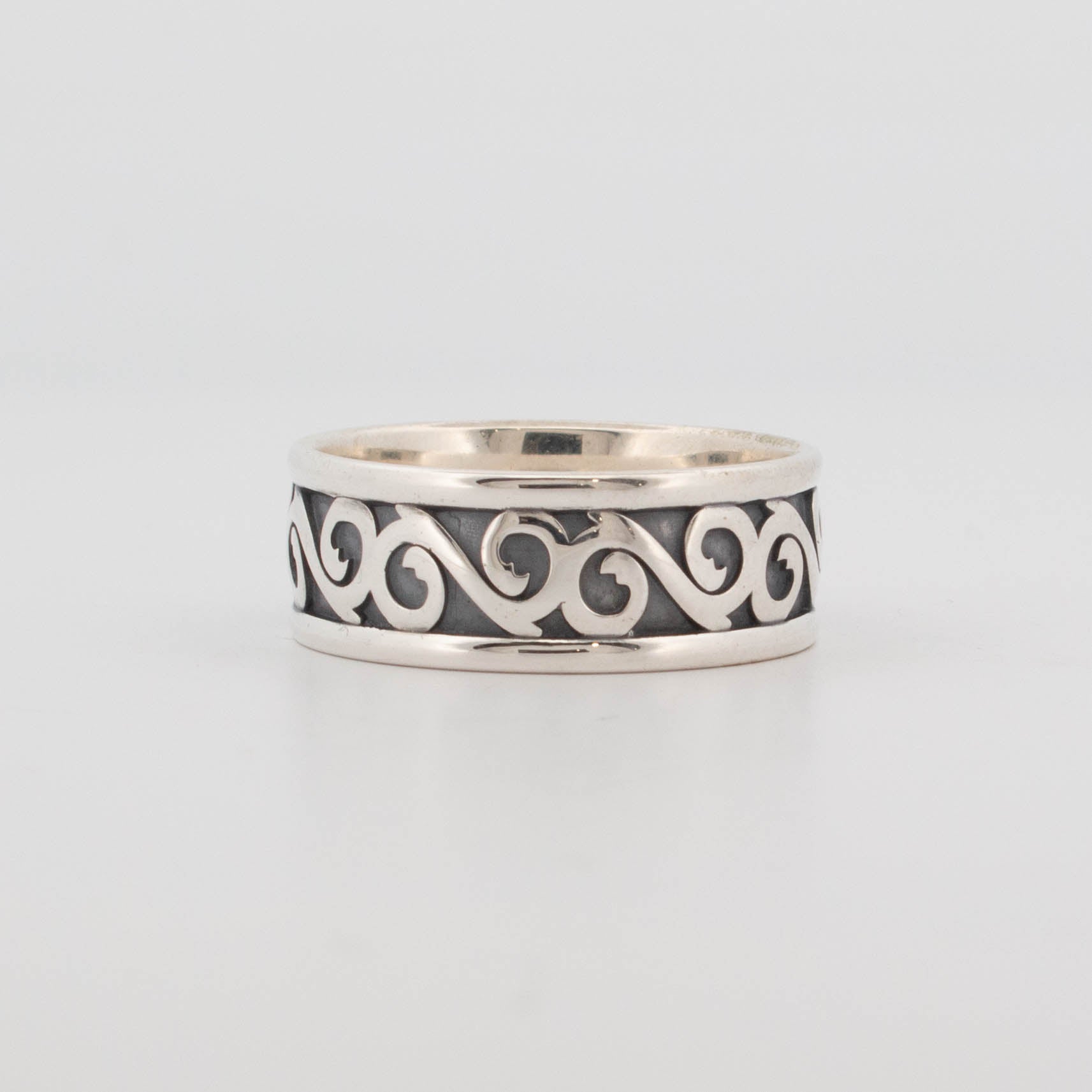 8mm wide sterling silver ring featuring raised swirl pattern on an oxidised blackened background, with polished edges; handcrafted band with baroque-style scrolling motif and dark patina contrast.