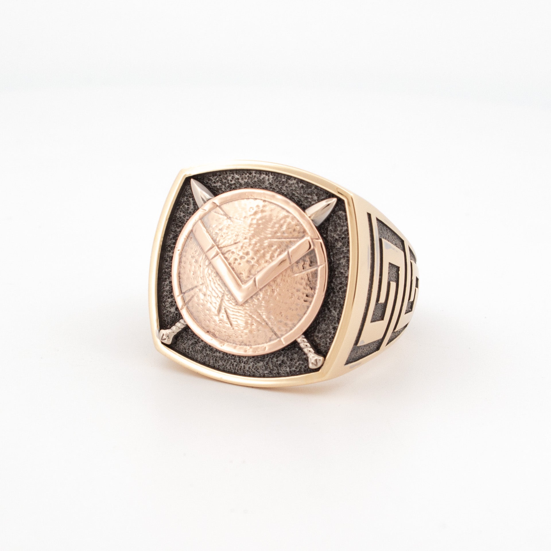 18ct recycled gold Spartan shield signet ring with yellow, rose, and white gold alloy, black rhodium detail, and Greek Key pattern on the shank.