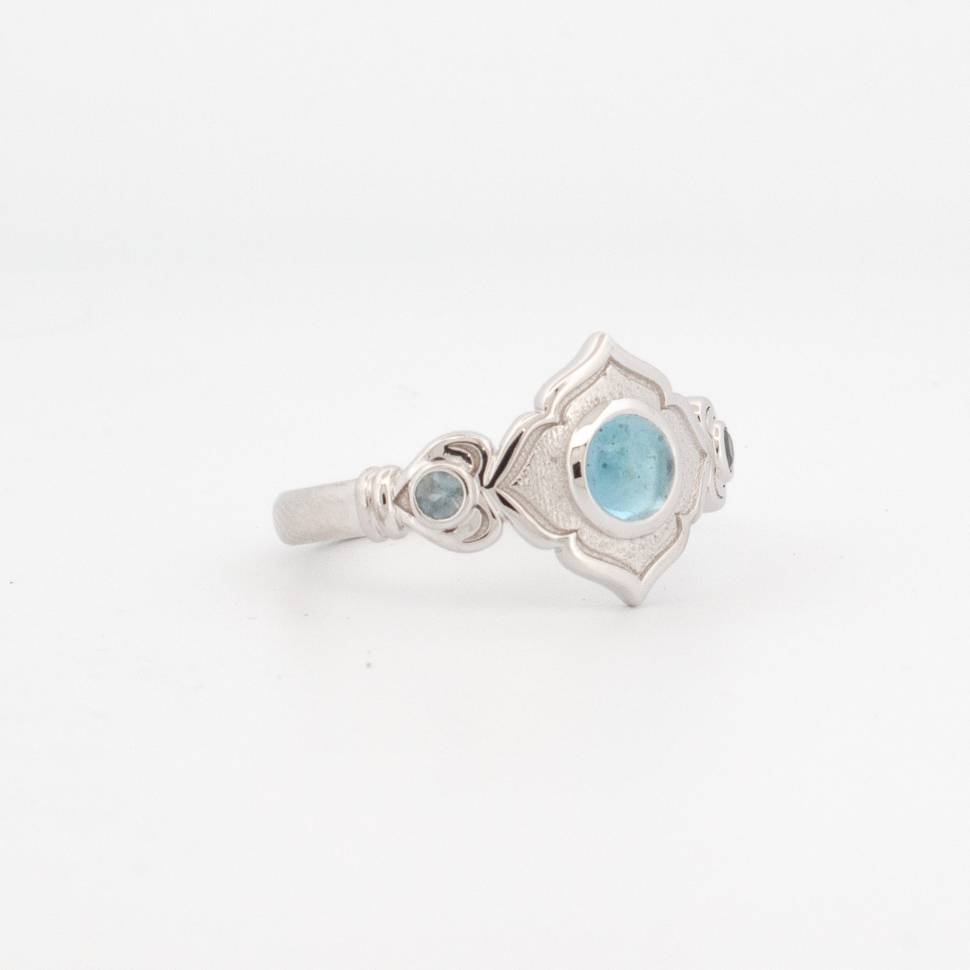 9ct white gold ring with 5mm round cabochon topaz and two bezel-set light blue sapphire shoulder stones in scalloped geometric setting.