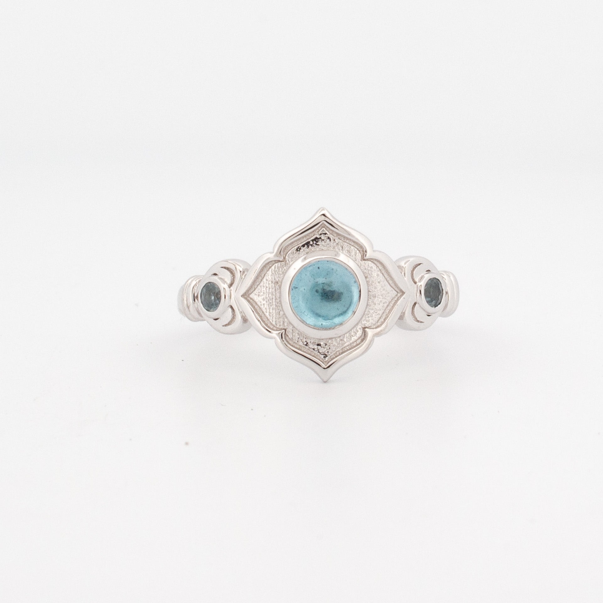 9ct white gold ring with 5mm round cabochon topaz and two bezel-set light blue sapphire shoulder stones in scalloped geometric setting.
