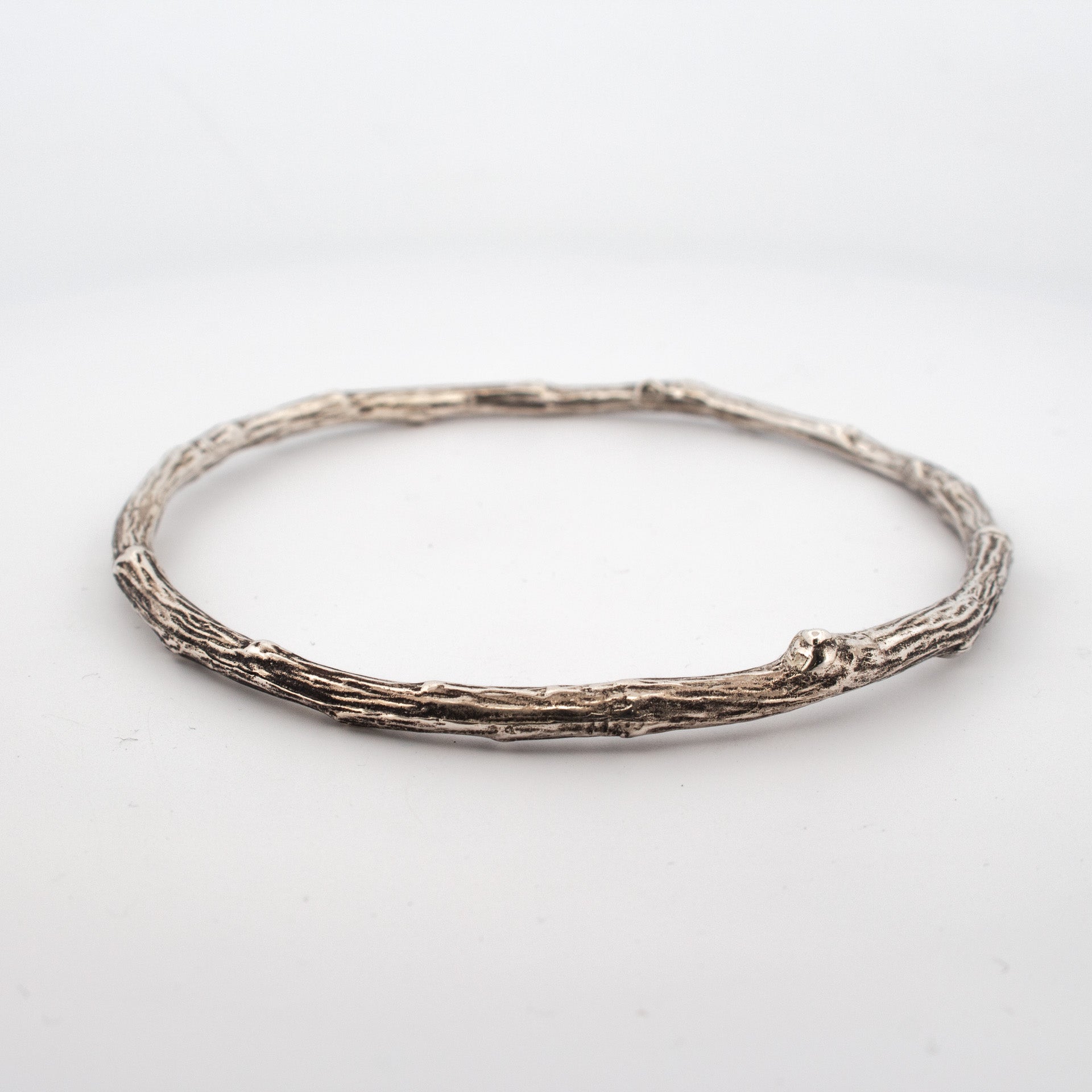 Sterling silver twig bangle with textured bark surface, organic round shape and natural knot detailing.
