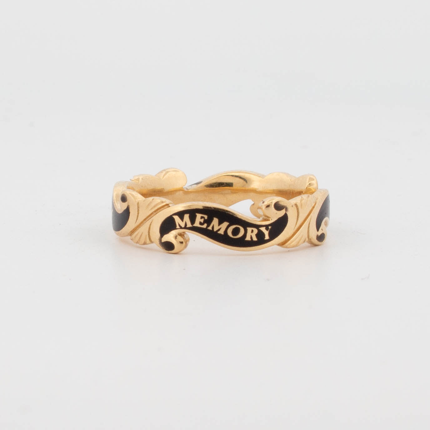 18ct yellow gold memorial ring with black enamel scrollwork, engraved with the inscription 'IN MEMORY OF CARL' around the band; designed as a tribute piece with ornate ribbon-like detailing.