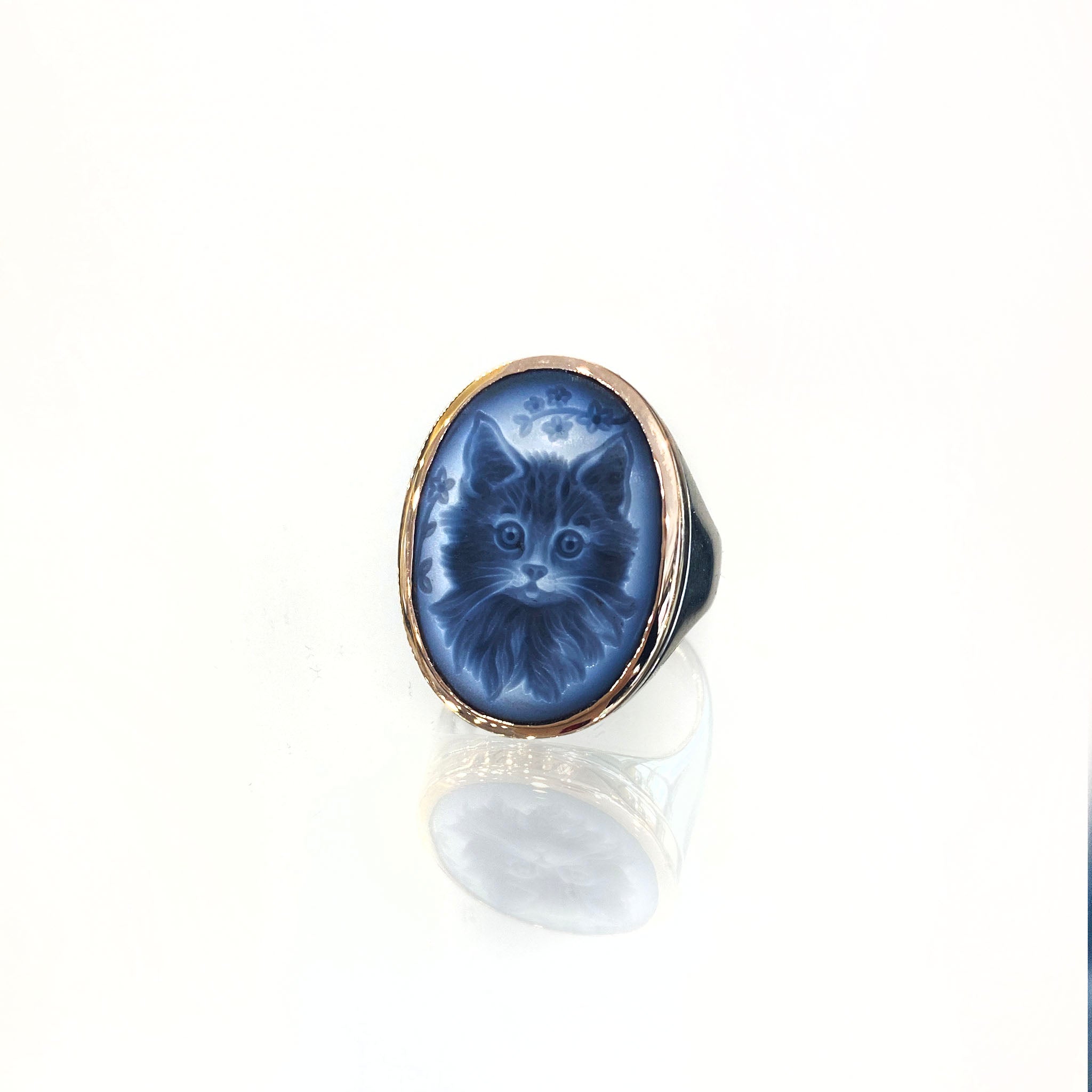 Rose gold and sterling silver cameo ring with oval bezel, featuring hand-carved kitten portrait with floral detailing on blue-toned background.