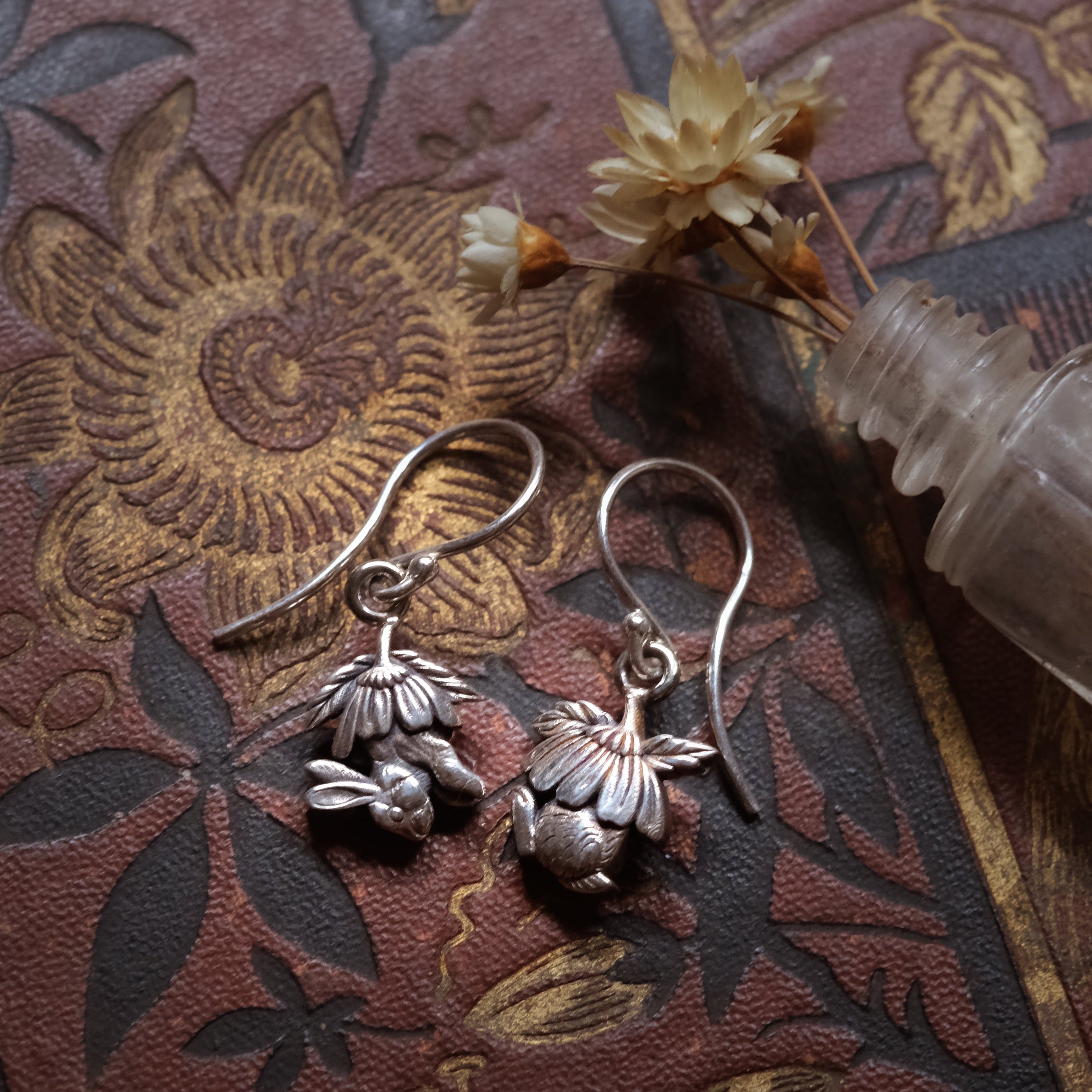 Sterling silver drop earrings with sculpted half bunny forms under layered daisy flower caps, handmade woodland jewellery