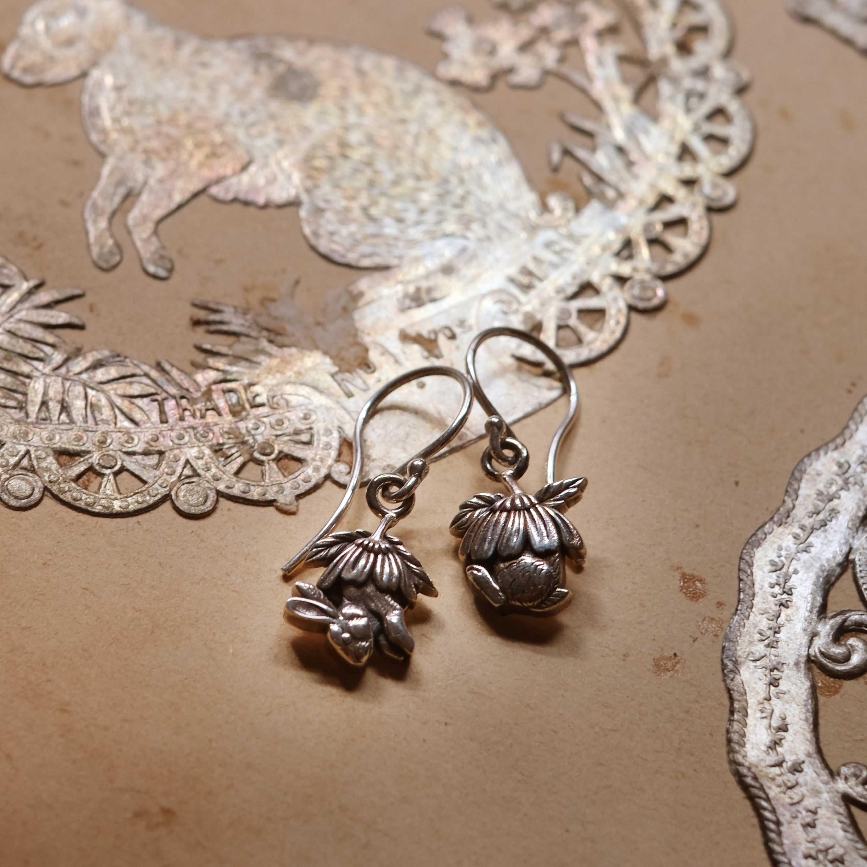 Sterling silver drop earrings with sculpted half bunny forms under layered daisy flower caps, handmade woodland jewellery