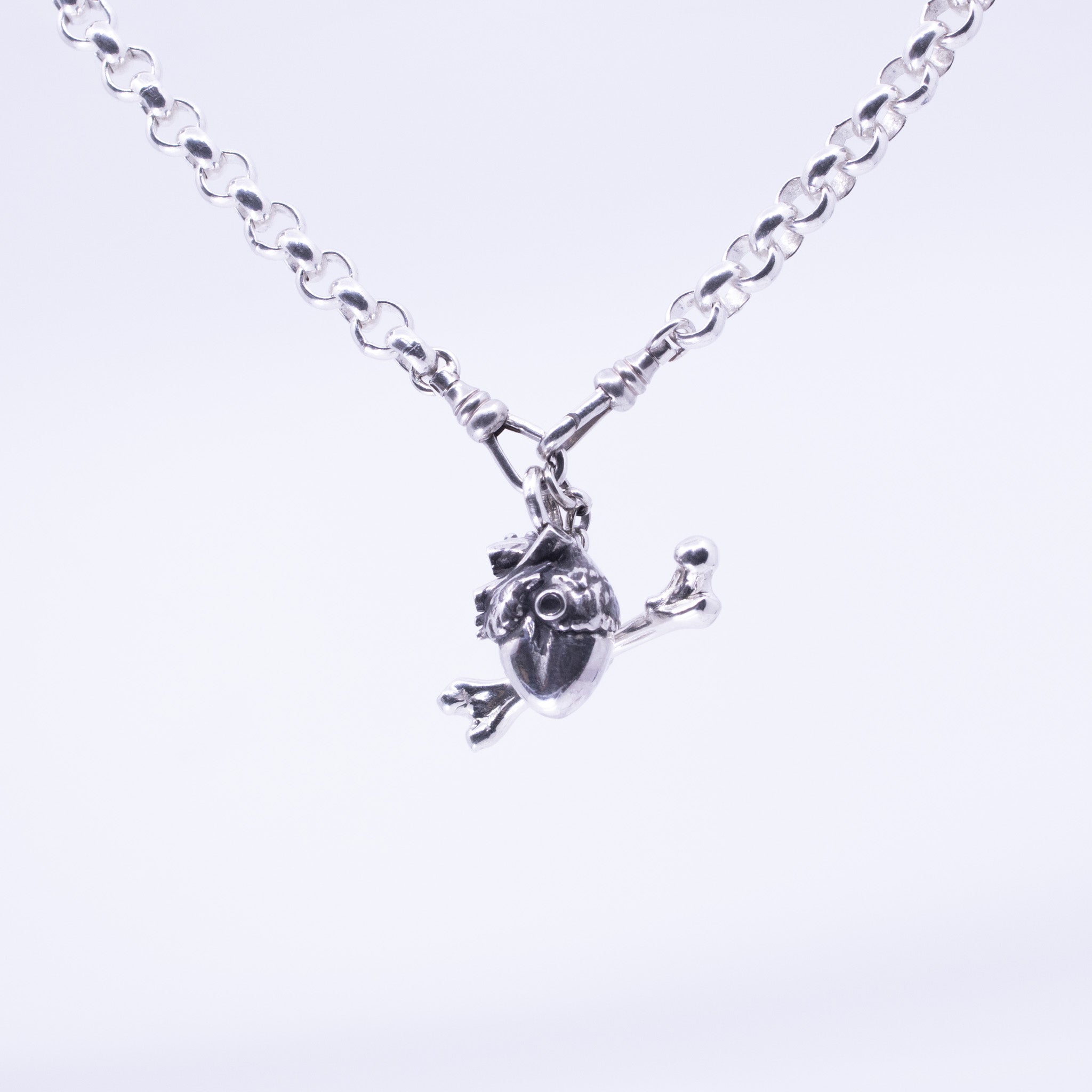 Sterling silver necklace with anatomical heart and crossbone charm, detailed with sculpted ventricles and arteries, suspended on a heavy silver chain with reinforced links.