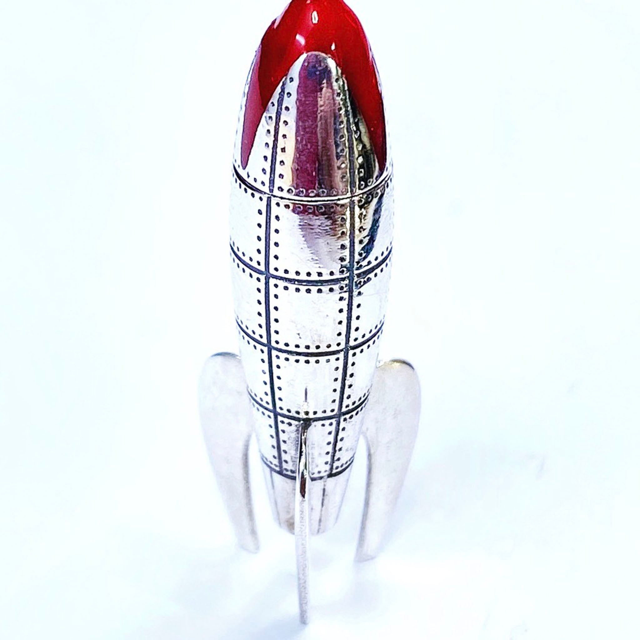 Sterling silver rocketship pendant with rivet panel detailing, red enamel nose cone, and three sculpted fins in retro sci-fi style.