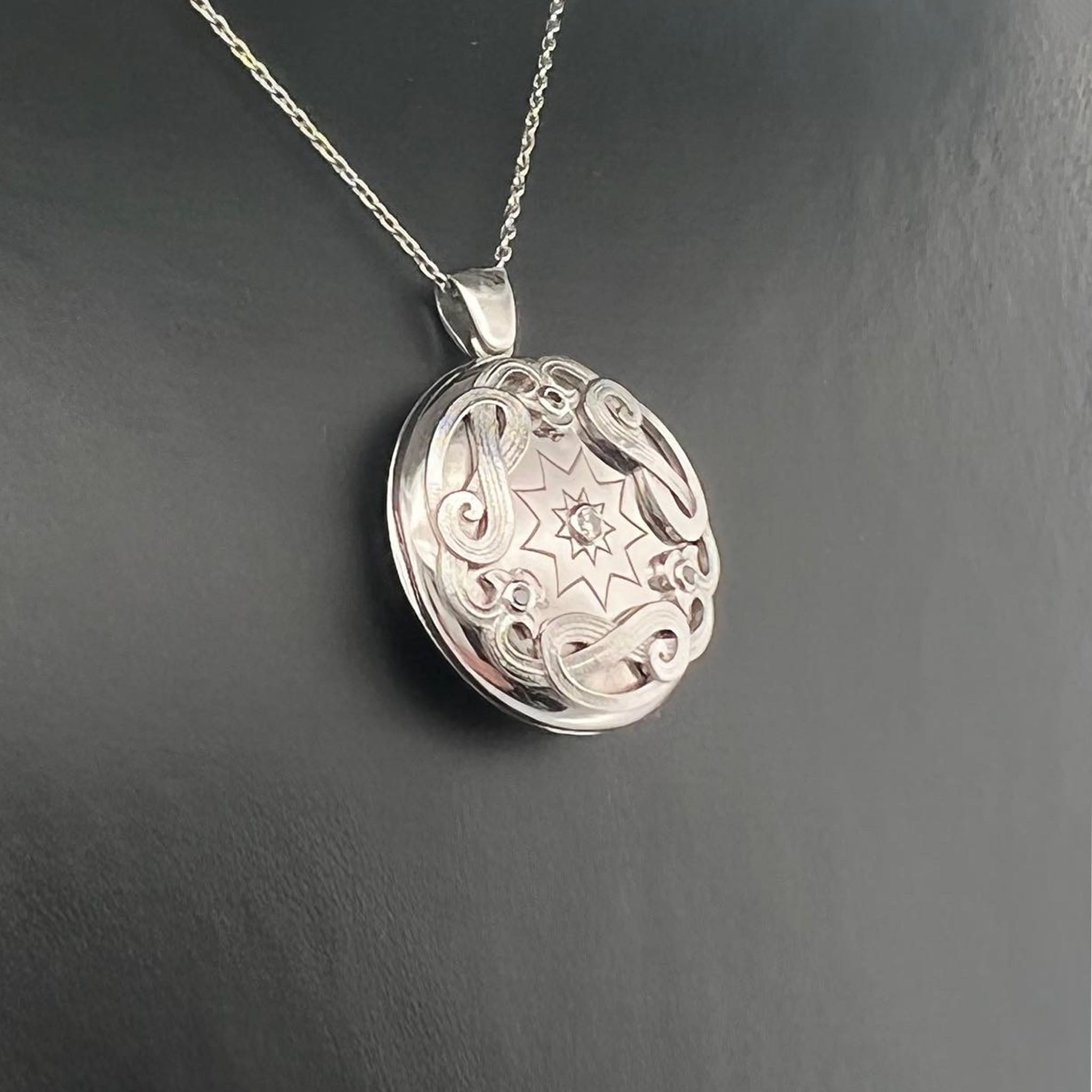 18ct white gold memorial locket pendant with engraved scrollwork border, central starburst engraving set with round brilliant cut diamond, suspended on fine chain.