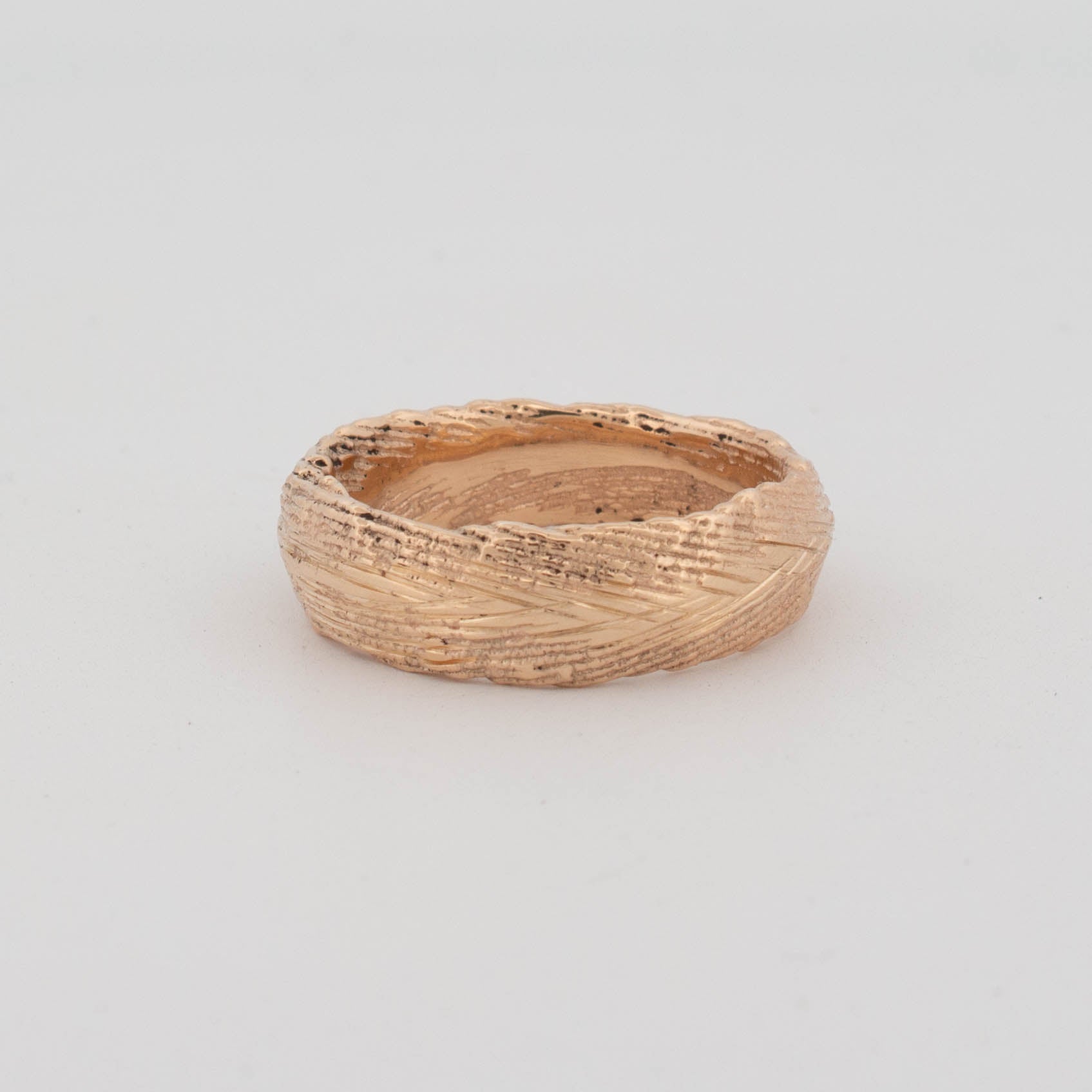Angled view of a 18ct yellow gold ring cast using a real cuttlefish bone mold, featuring an organic, linear texture with natural grooves and ridges across the band. The surface shows uneven, tactile striations unique to cuttlefish casting, creating a raw, sculptural form with a matte-meets-polished finish.