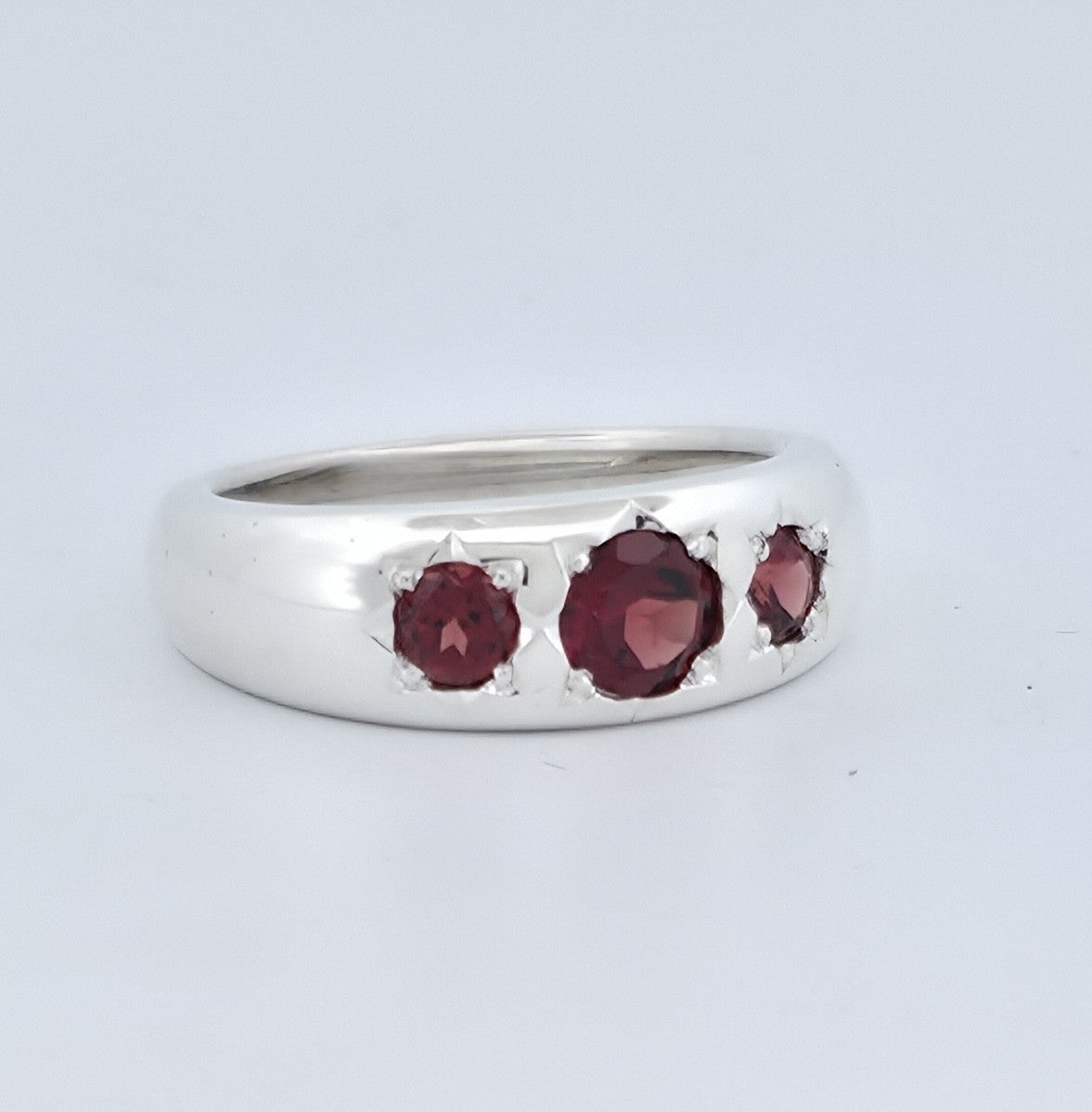 Polished silver statement ring featuring three round, deep-red garnets in hand-finished settings, with a larger centre stone flanked by two smaller stones.