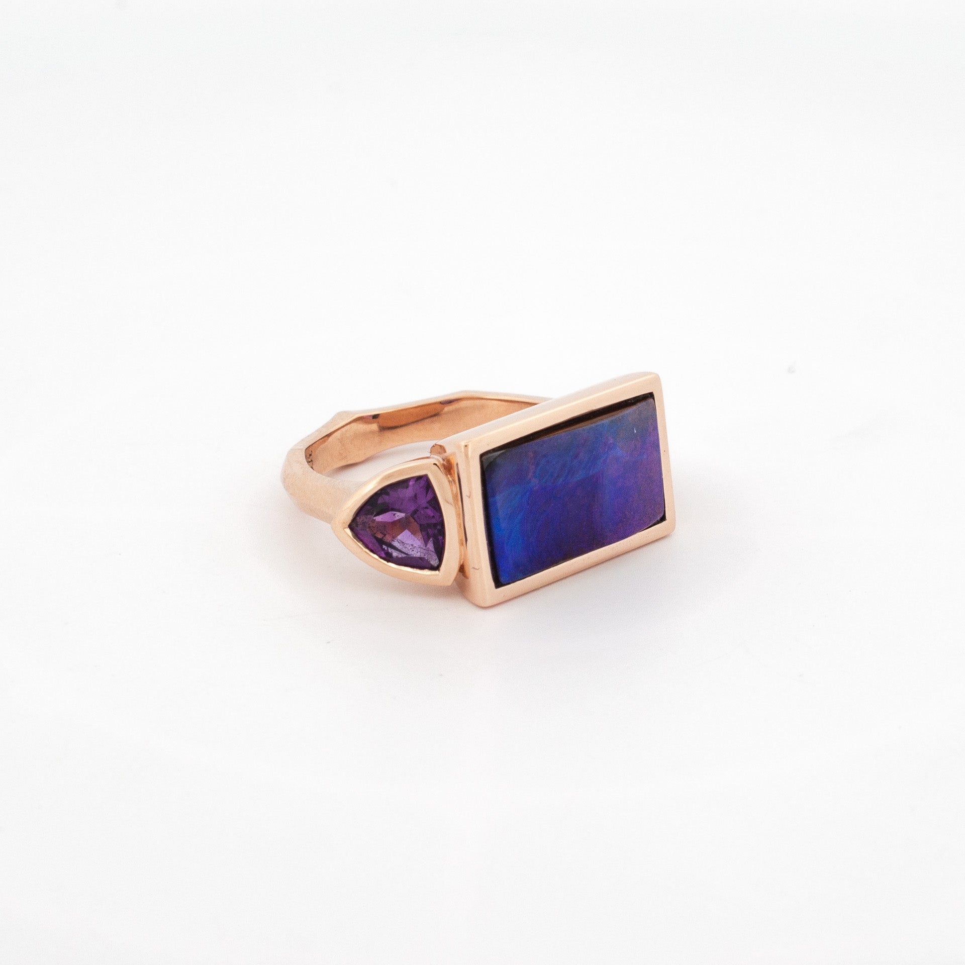 A rose gold ring featuring a central Australian Boulder Opal with purple amethyst side stones on either side.