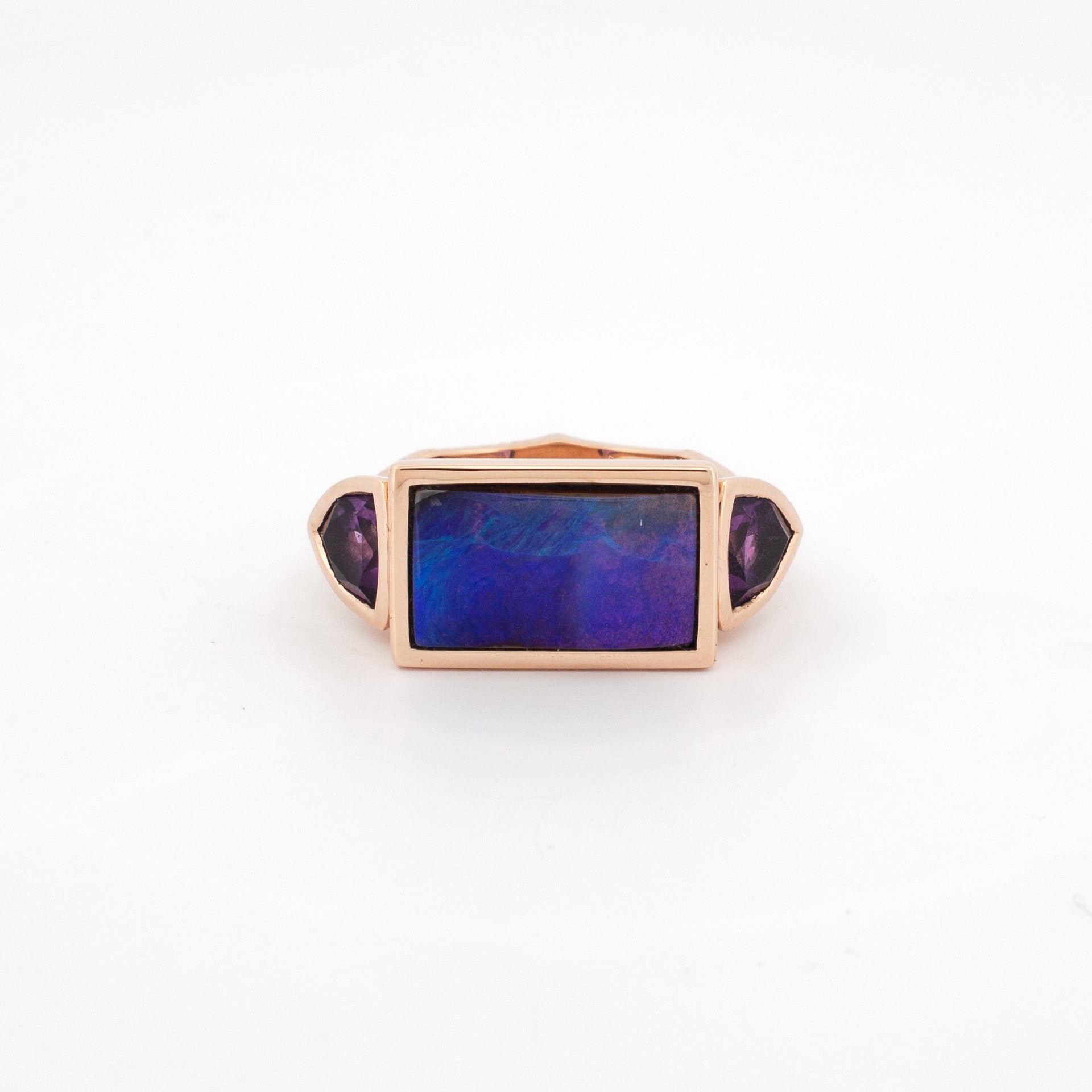 A rose gold ring featuring a central Australian Boulder Opal with purple amethyst side stones on either side.