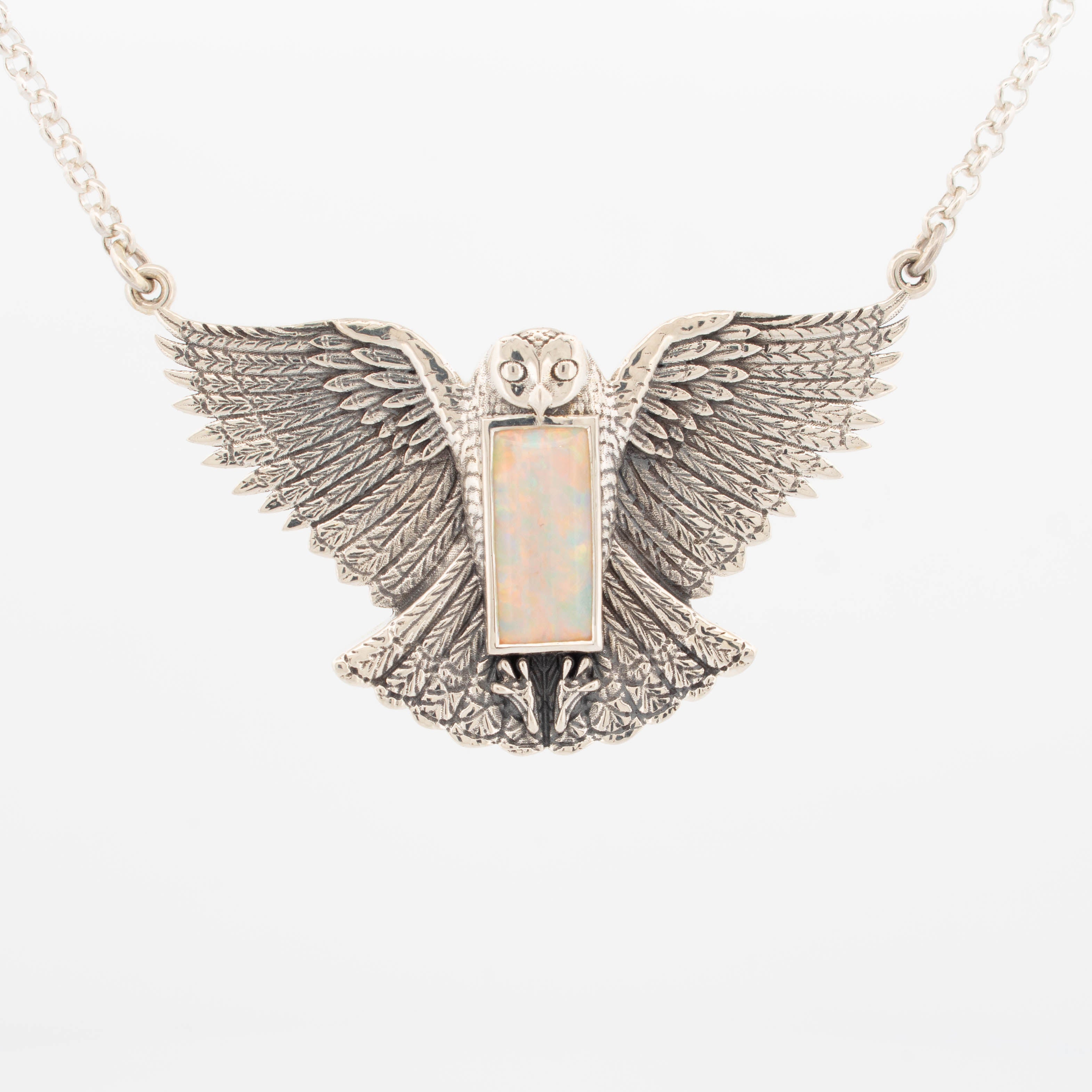 Intricately detailed snowy owl pendant crafted in sterling silver, featuring outstretched wings and a rectangular bezel-set Australian opal at the centre; suspended on a fine silver chain.