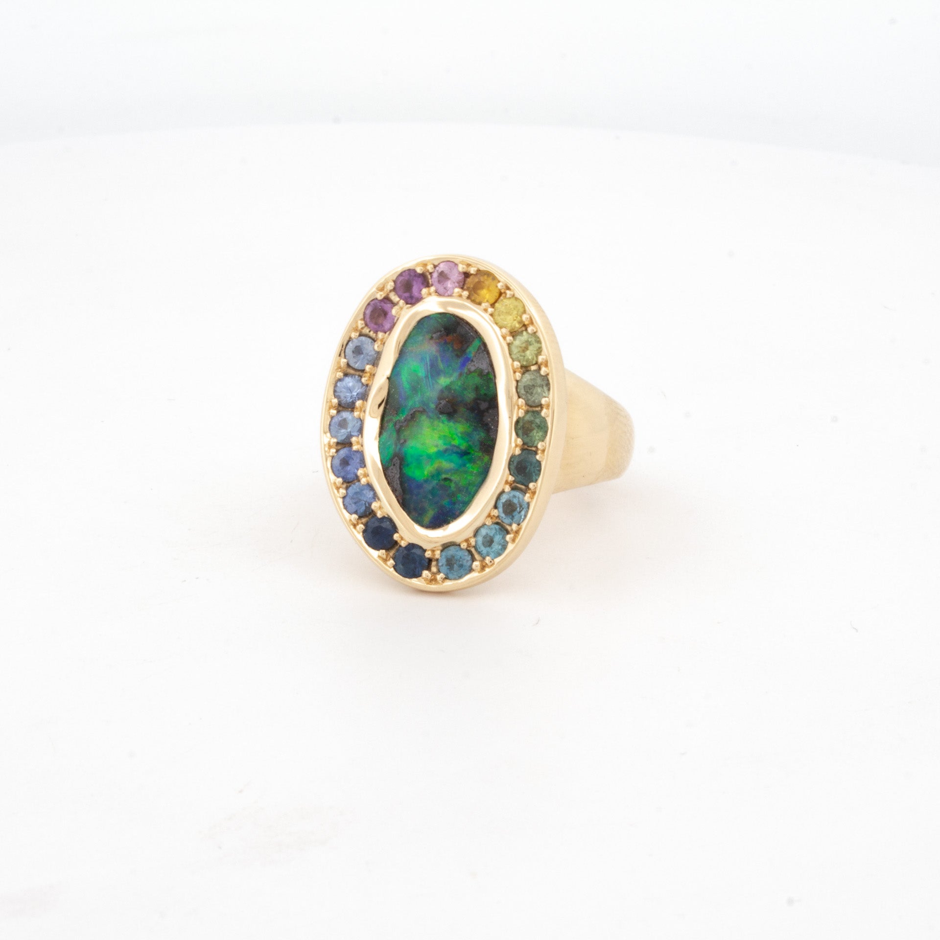 18ct yellow gold ring featuring boulder opal centre stone surrounded by rainbow-hued sapphires in oval bezel setting.