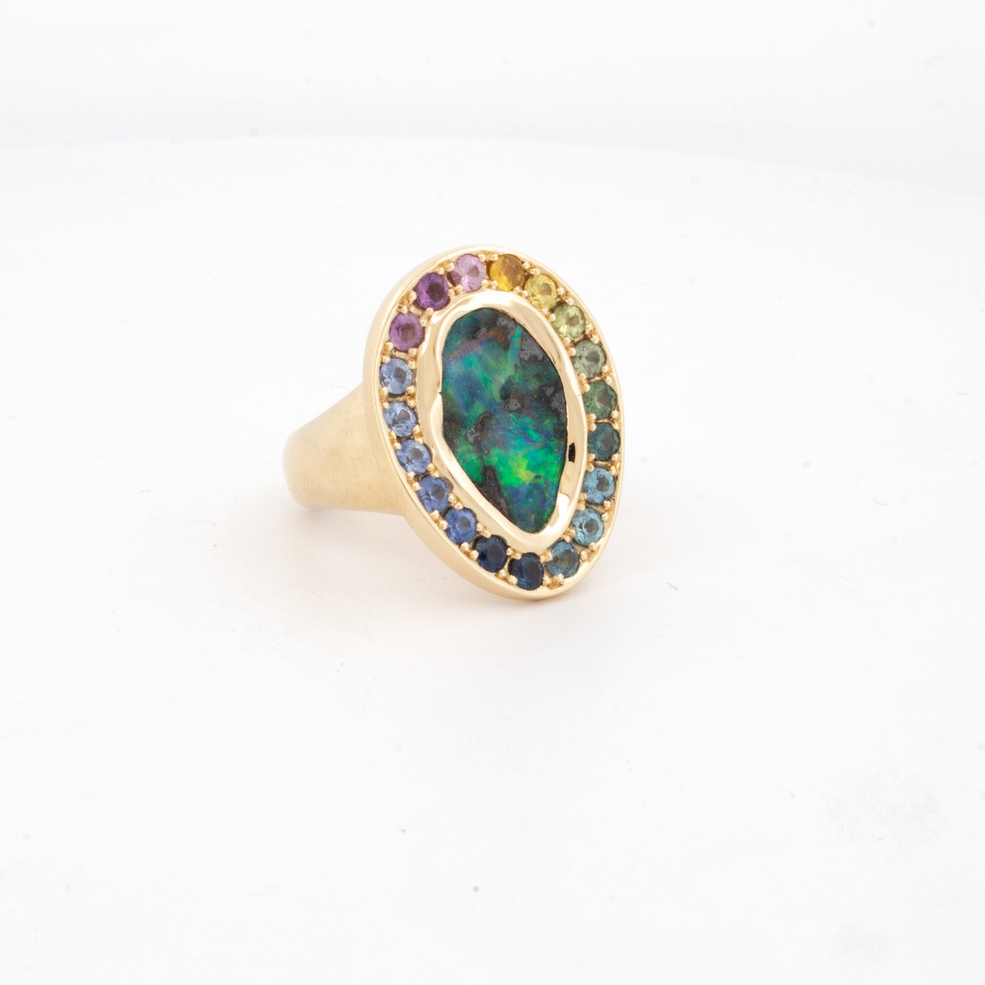 18ct yellow gold ring featuring boulder opal centre stone surrounded by rainbow-hued sapphires in oval bezel setting.