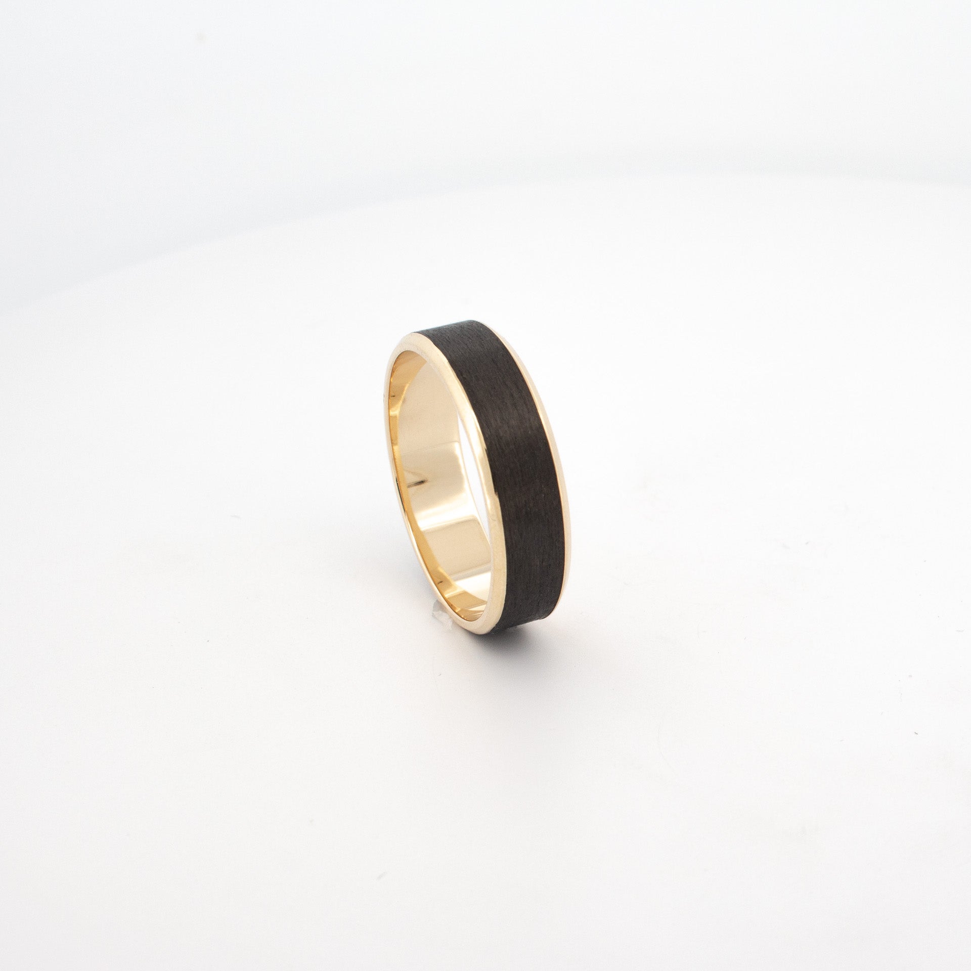 18ct yellow gold ring with inlaid black carbon fibre centre, flat profile and polished edges, modern men’s wedding band