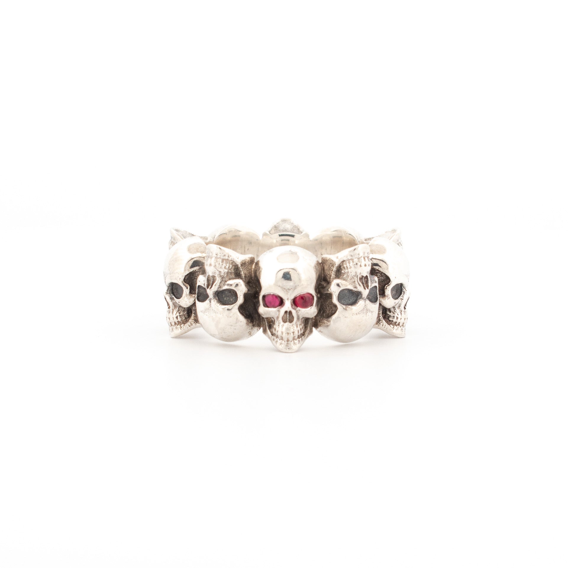 Sterling silver skull ring with continuous band of oxidised skulls and central skull set with cabochon ruby gemstone eyes.