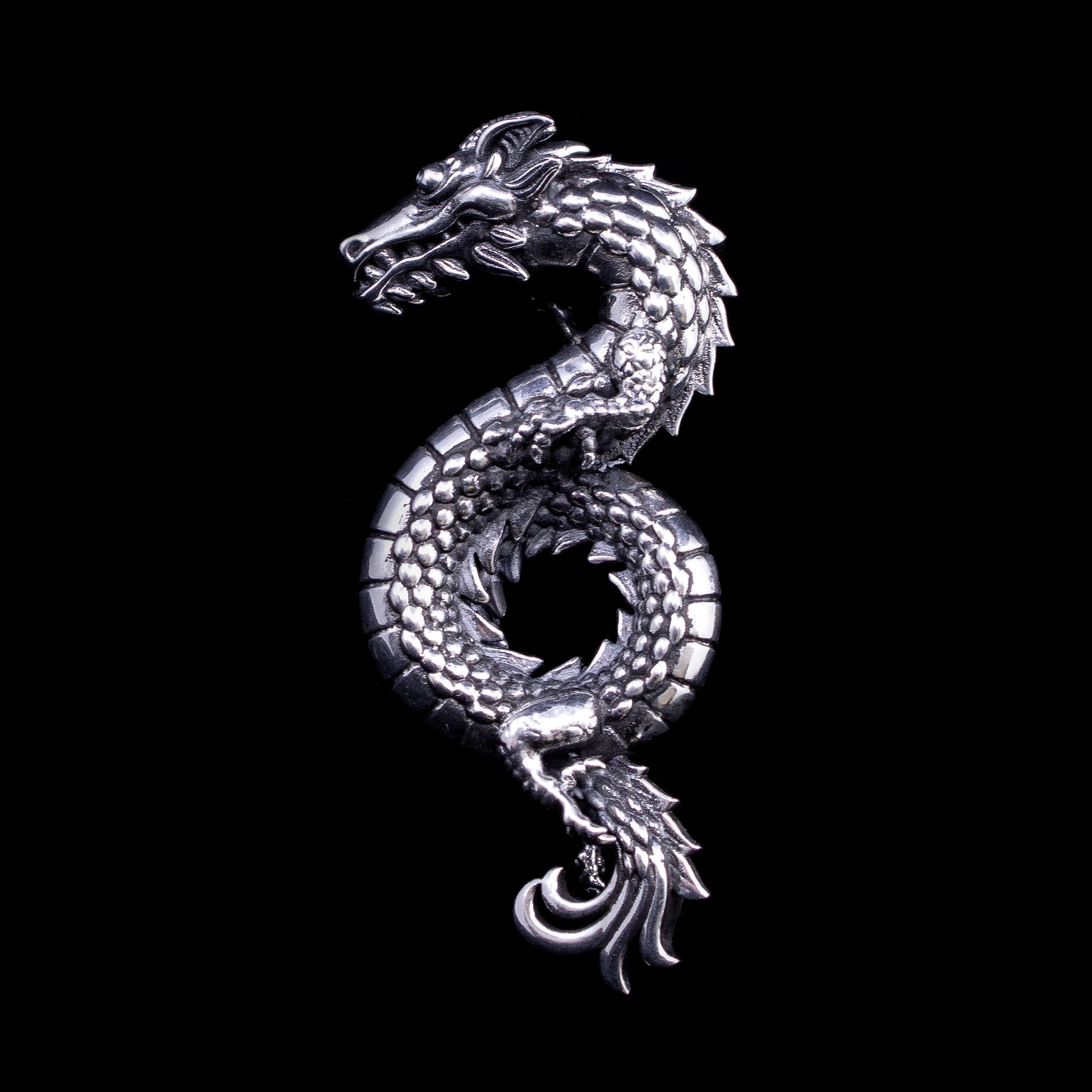 Sterling silver dragon memorial brooch with detailed sculpted scales, claws, and flowing tail, coiled into circular form with raised head and open jaw.