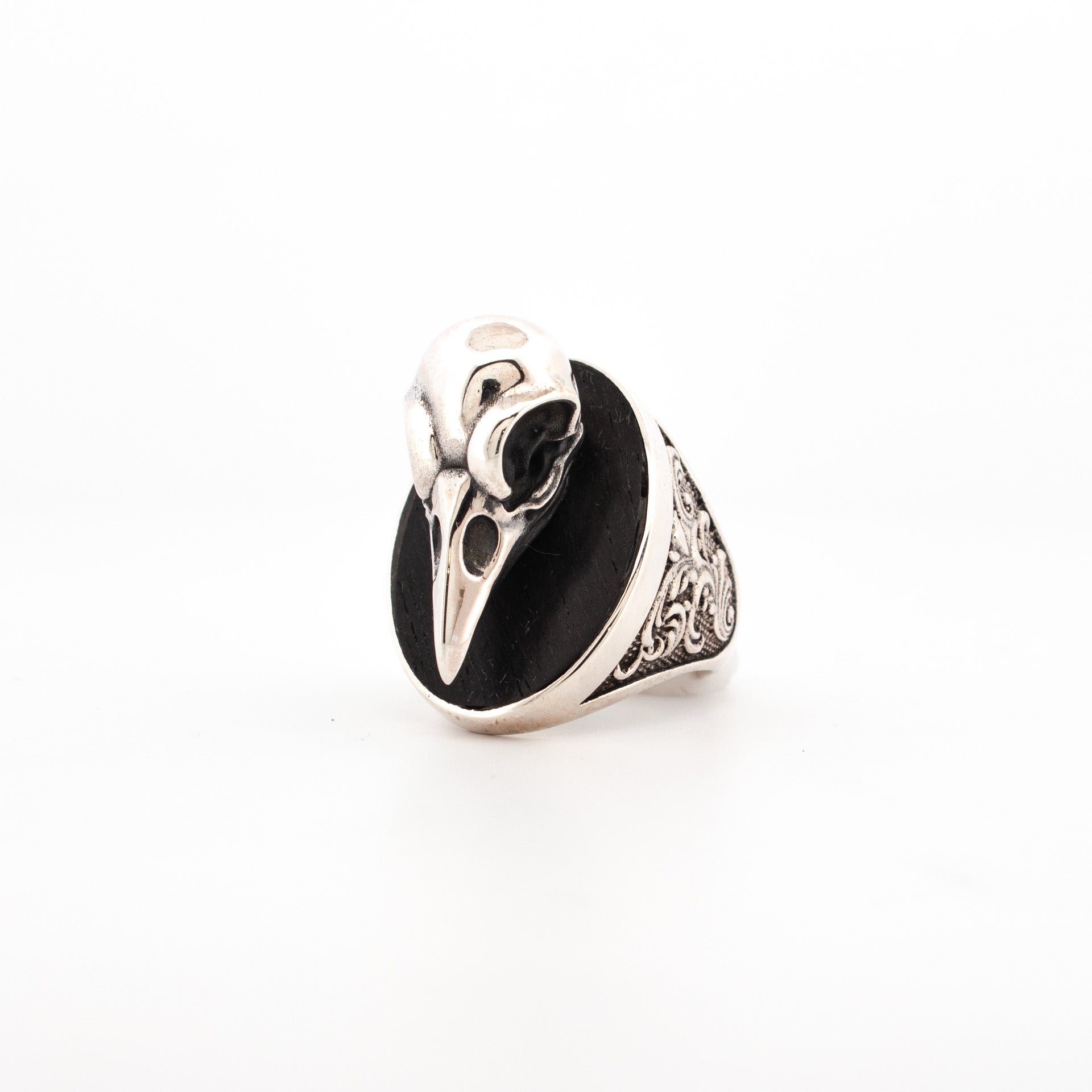 Sterling silver ring featuring sculpted raven skull over oval ebony inlay with engraved scrollwork shoulders.