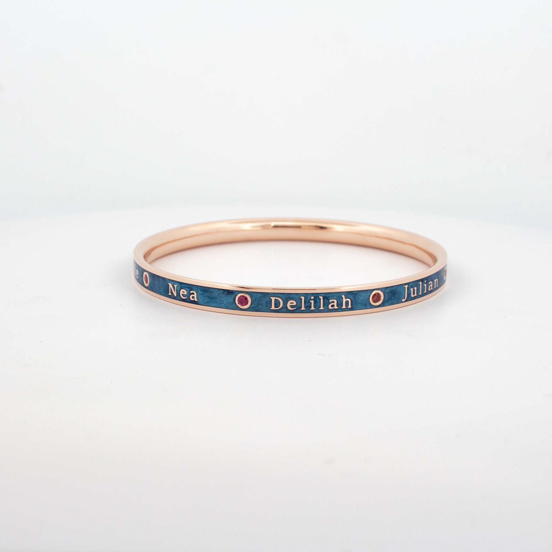 Custom rose gold bangle with blue enamel inlay, engraved names and bezel-set rubies.