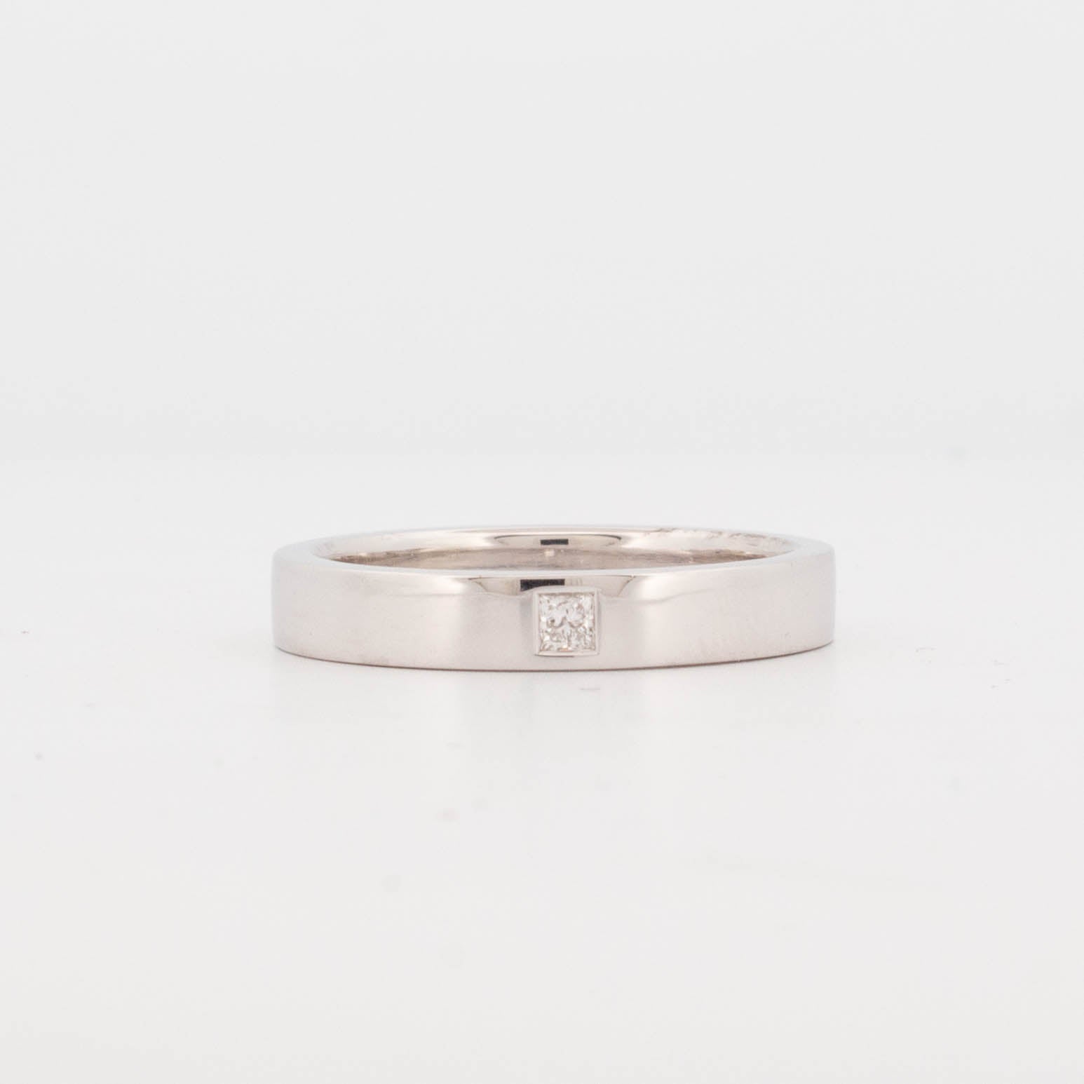 Straight-on view of a 9ct white gold ring with a flat, rectangular band profile and polished finish. Features a centrally placed, flush-set princess-cut white diamond in a precision-milled square seat. The ring exhibits uniform band thickness, clean edges, and a low-profile setting for durability and everyday wear. Ideal for modern unisex or minimalist wedding and commitment rings.