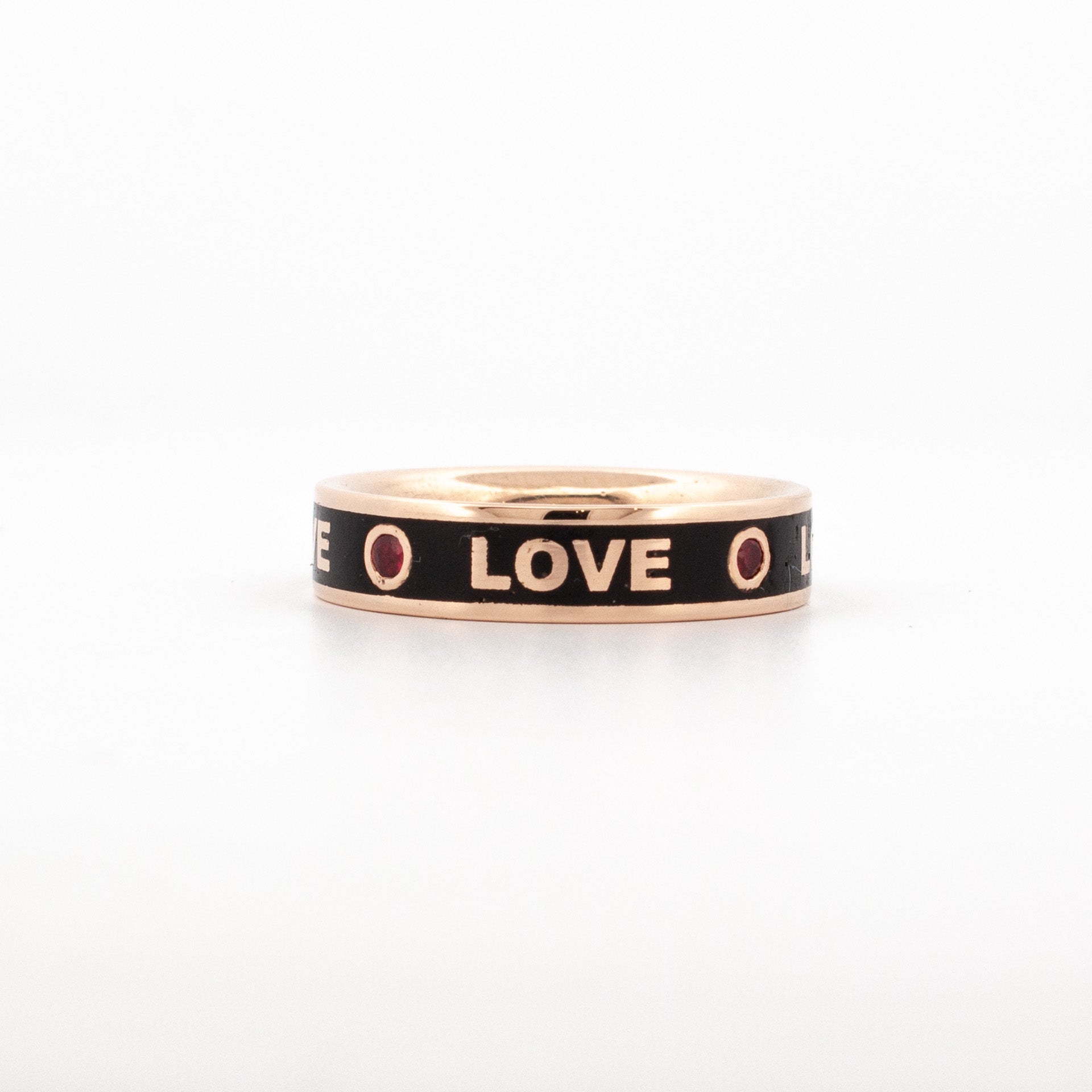 Crafted in 9ct rose gold, this band features bold black enamel detailing with the word LOVE repeating around the ring. Each “O” is set with a round-cut ruby, adding vibrant contrast to the design.