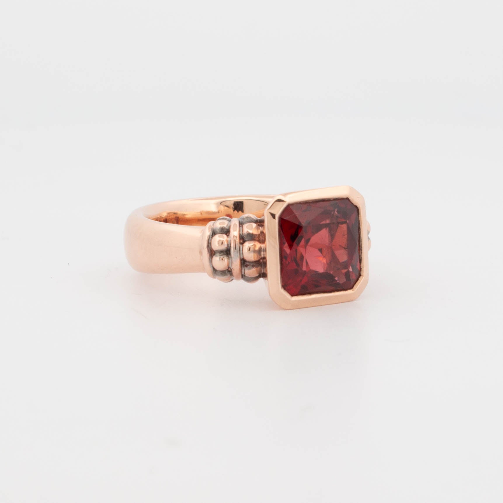 Side view of a 9ct rose gold ring featuring a square step-cut garnet in a bezel setting elevated above the band. The setting reveals a structured profile with oxidised granule detailing on each shoulder, adding texture and contrast. The band is slightly domed with a smooth polish, showcasing balanced proportions and a low-profile silhouette designed for comfortable, everyday wear.