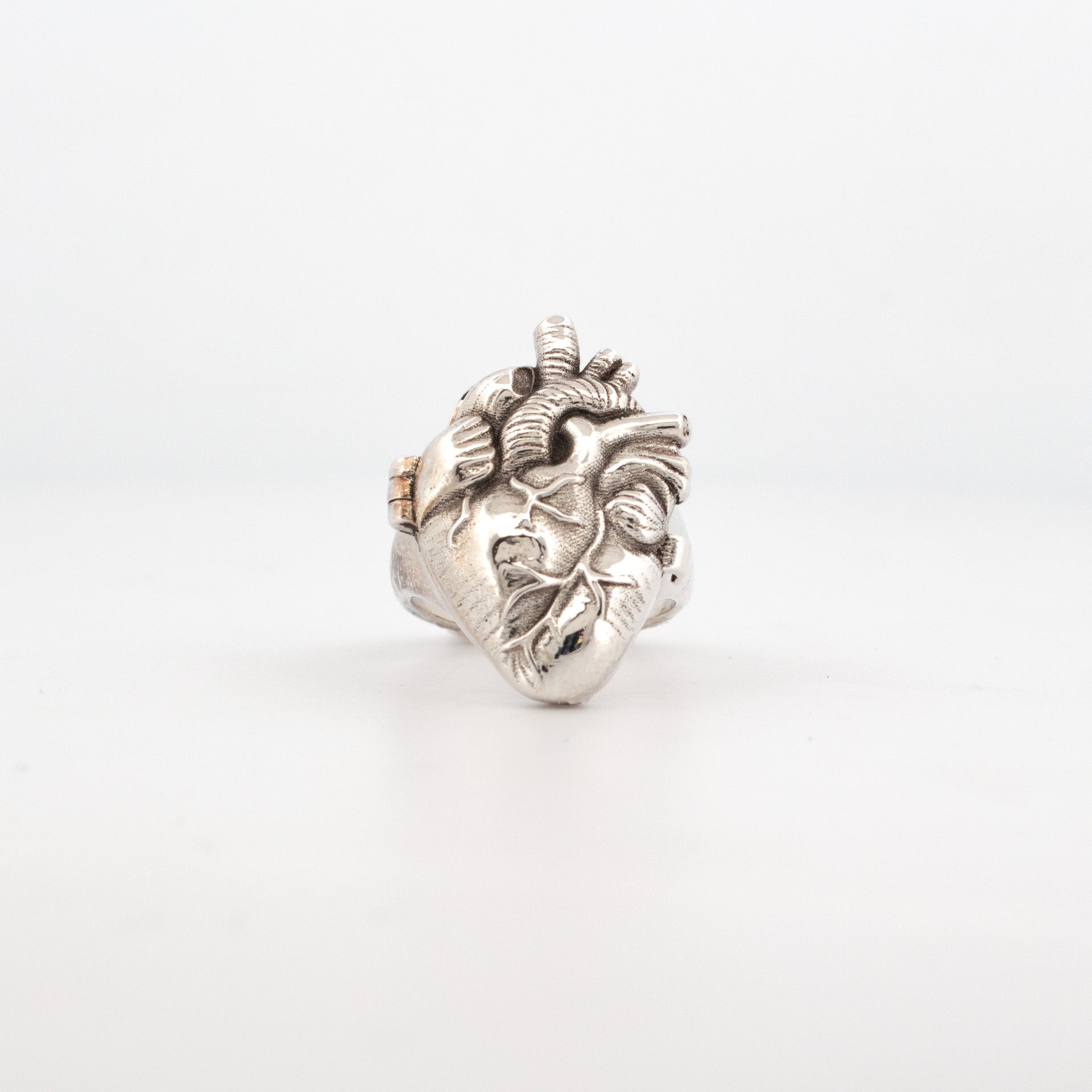 A sterling silver anatomical heart-shaped ring with a blood red enamel interior, displayed against a white background.