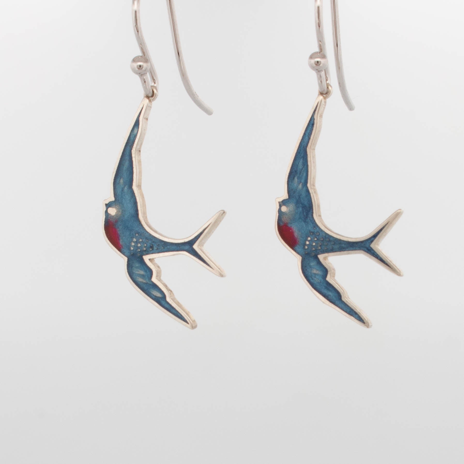 Sterling silver drop earrings featuring stylised bluebird silhouettes with hand-applied blue and red enamel detailing, suspended from polished hook ear wires; lightweight, handcrafted bird-themed jewellery ideal for nature lovers and everyday wear.