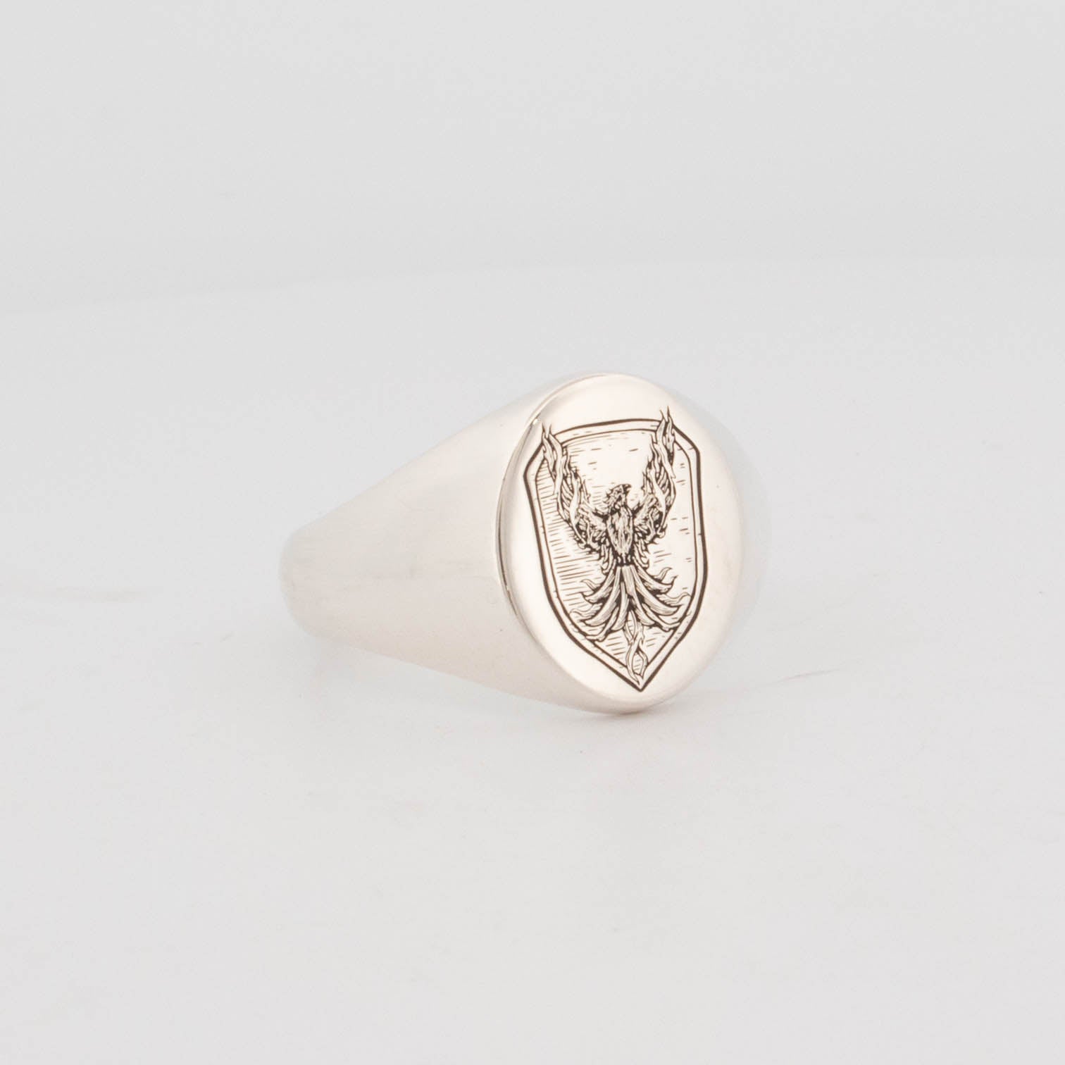 Sterling silver signet ring with engraved phoenix rising from flames, set within a shield-shaped crest on a polished oval face; bold mythological design, sold as-is with no customisation.