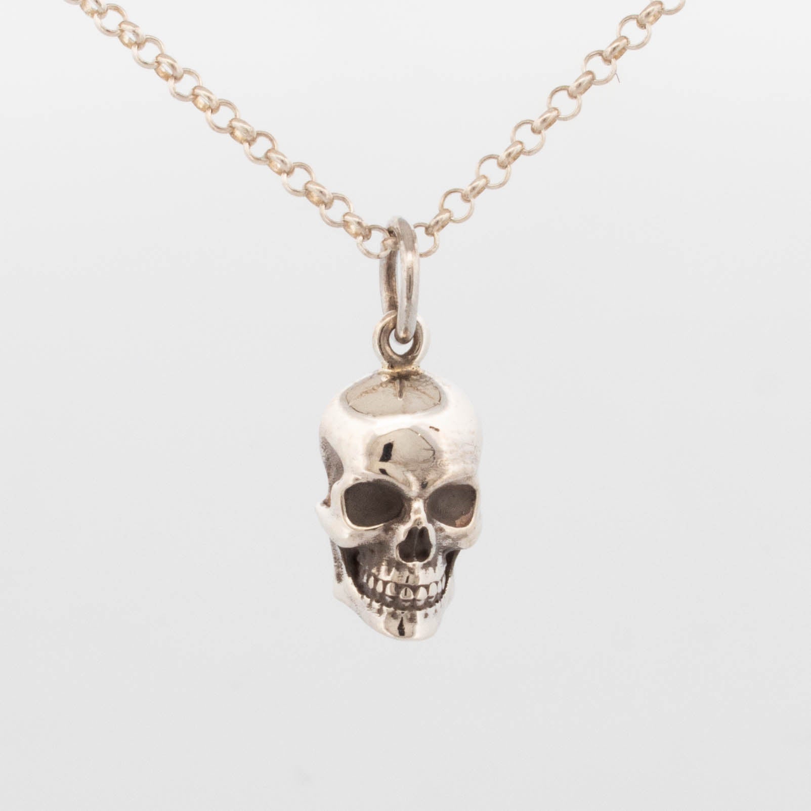 Sterling silver skull pendant with hollowed eye sockets and detailed teeth, suspended from a fine cable chain; handcrafted gothic-style necklace with anatomical realism and oxidised shadowing.