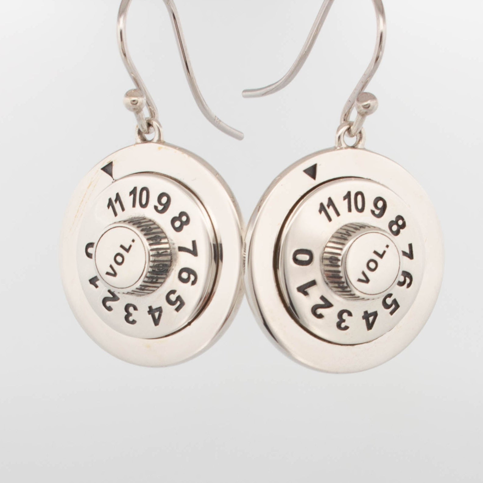 Sterling silver drop earrings shaped like vintage amplifier volume knobs, with engraved numbers 0–11 and “VOL.” text, crafted in high-polish silver with curved hook ear wires; novelty music-themed jewellery for audiophiles and retro rock lovers.