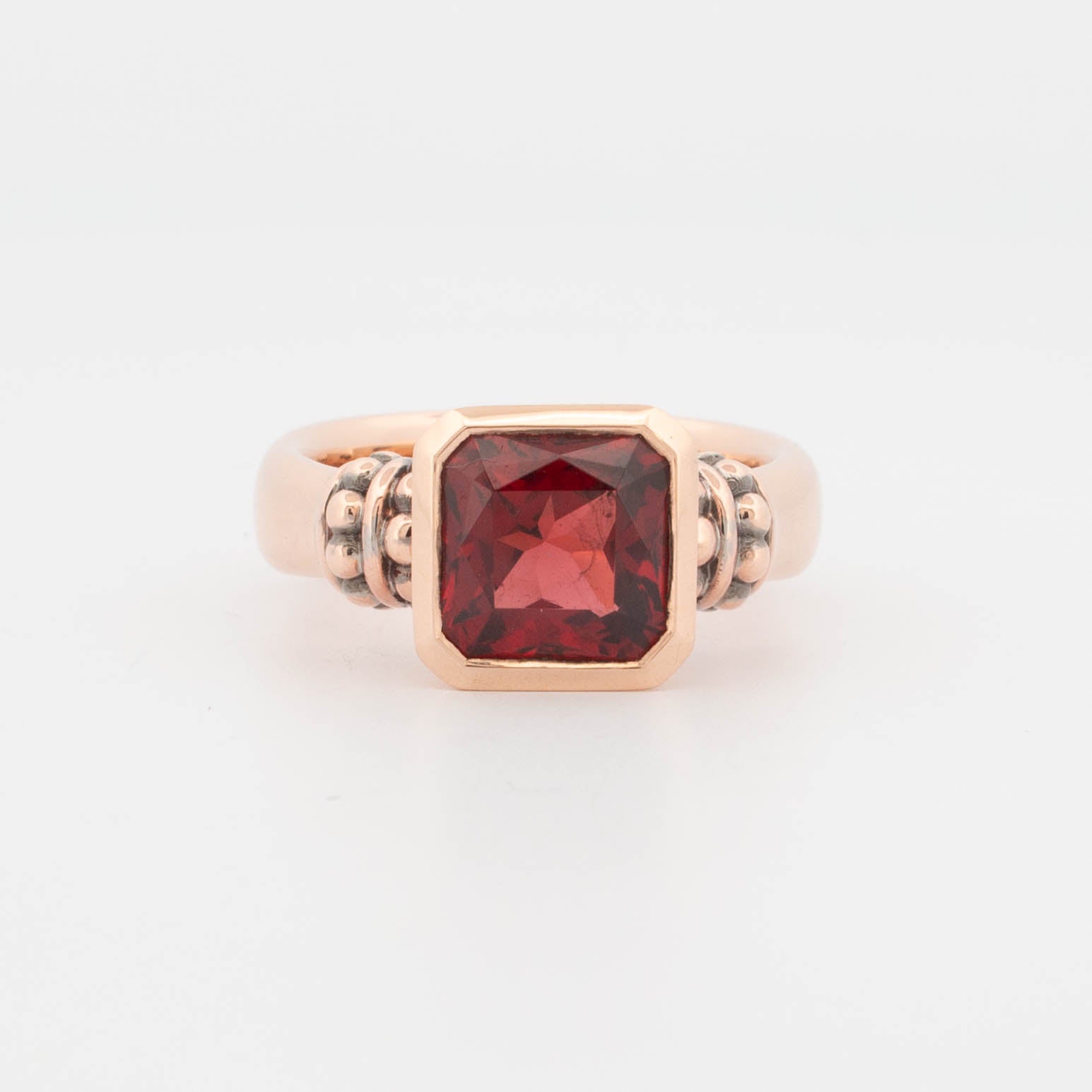 Front view of a handcrafted 9ct rose gold ring featuring a square step-cut deep red garnet in a bezel setting. The gemstone is flanked by oxidised granule detailing on each side of the setting, enhancing the vintage-inspired architectural design. Polished domed band with balanced proportions, combining bold colour with structural elegance in fine gemstone jewellery.