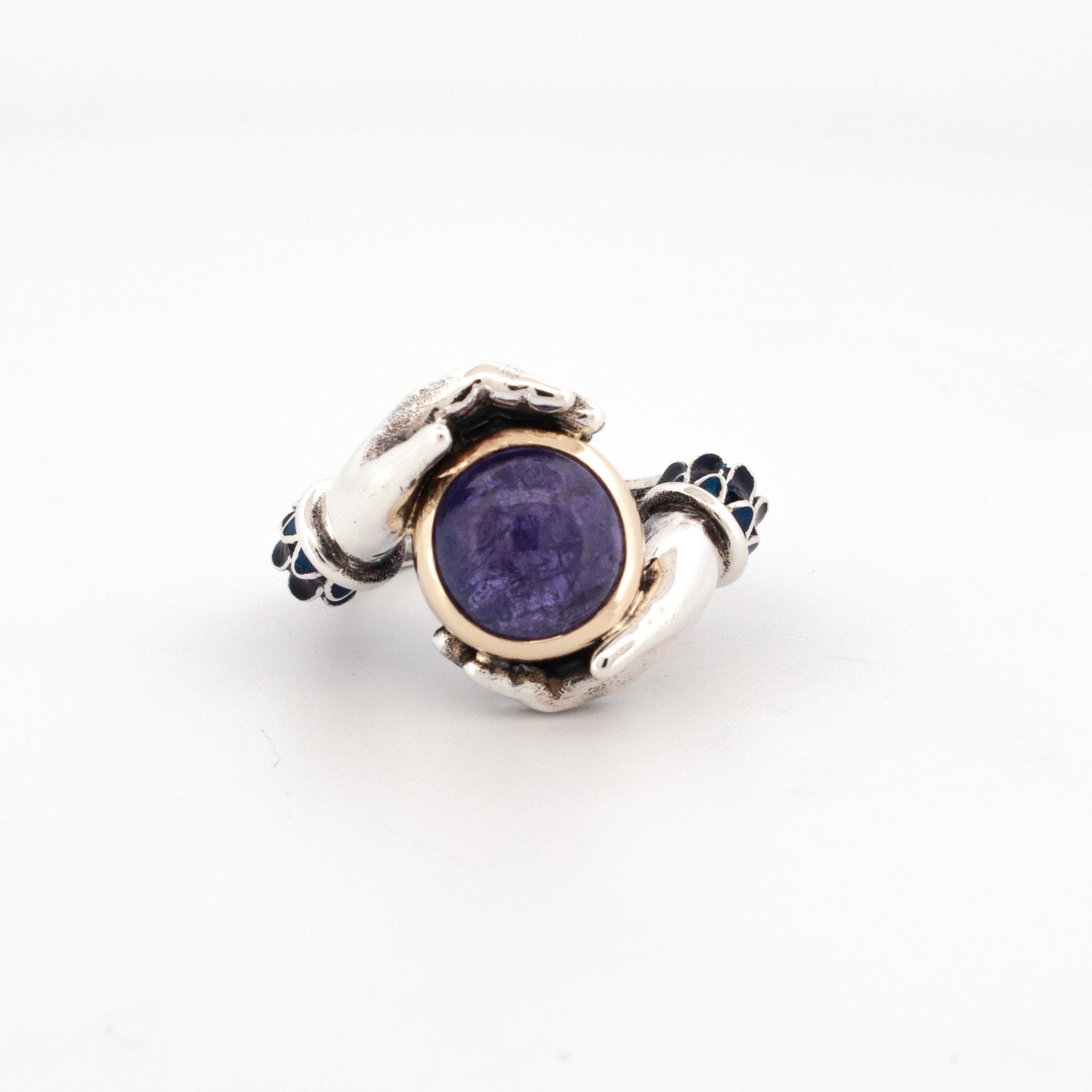 Sterling silver ring with enamelled sleeves and 9ct yellow gold bezel set 10mm round cabochon tanzanite, held by sculpted hands.