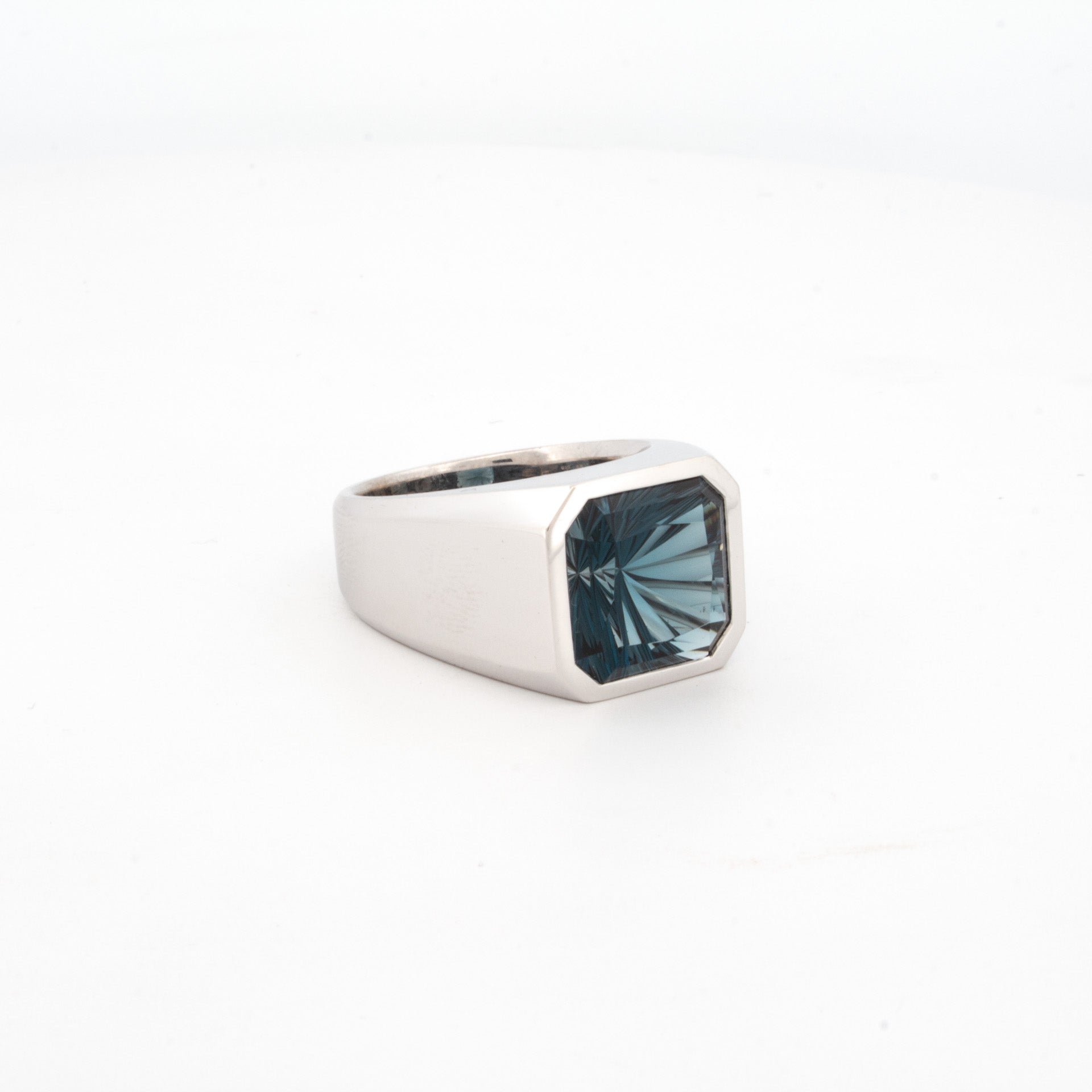 side view of 9ct white gold signet ring with octagonal bezel set custom-cut London Blue Topaz featuring concave warp-style faceting.