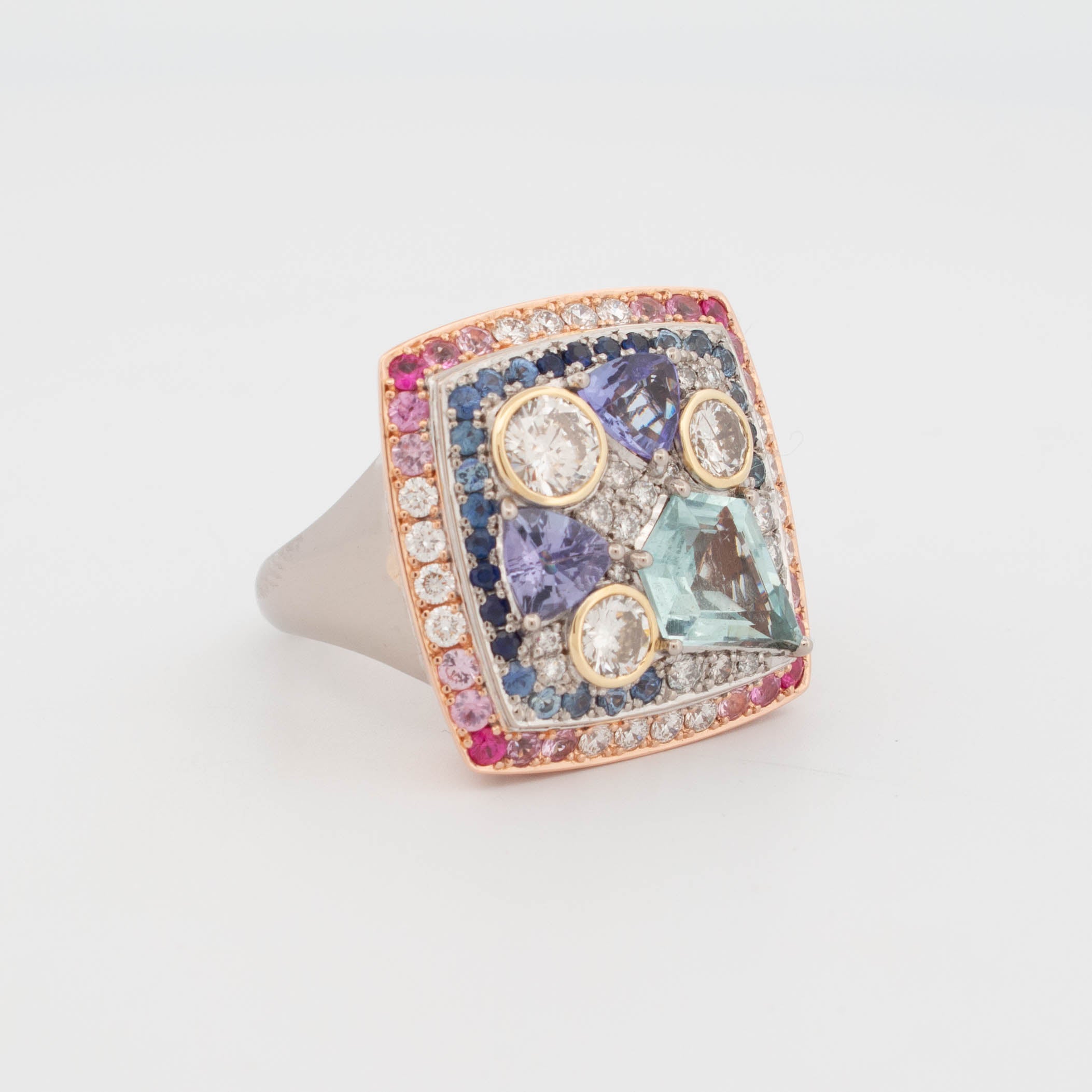 Handmade 18ct rose, white, and yellow gold ring featuring central aquamarine in geometric cut, tanzanite in triangular cuts, round brilliant cut diamonds in yellow gold bezels, and pavé-set colour fade sapphires transitioning from pink to blue.