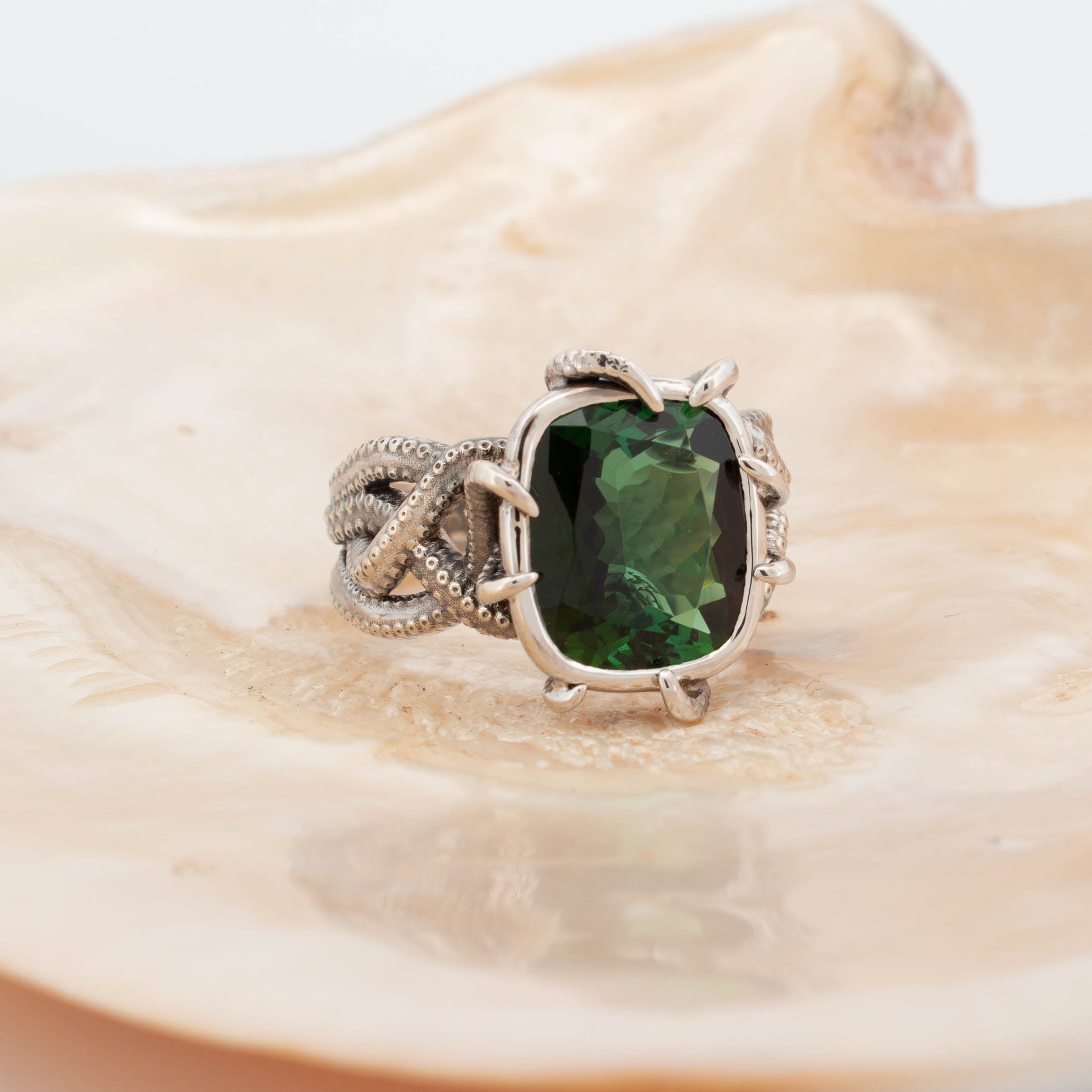 9ct white gold ring featuring a large cushion-cut green tourmaline held in claw prongs, with intricately sculpted octopus tentacles forming the band and detailed with textured suction cups.