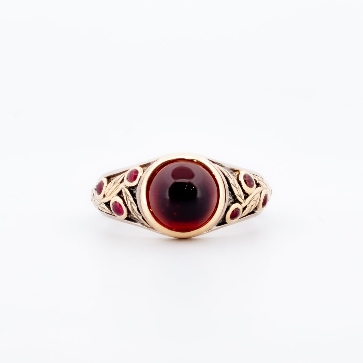 18ct yellow and white gold ring featuring a central round cabochon garnet and bezel-set rubies in a leaf-engraved band design, inspired by pomegranate hues.