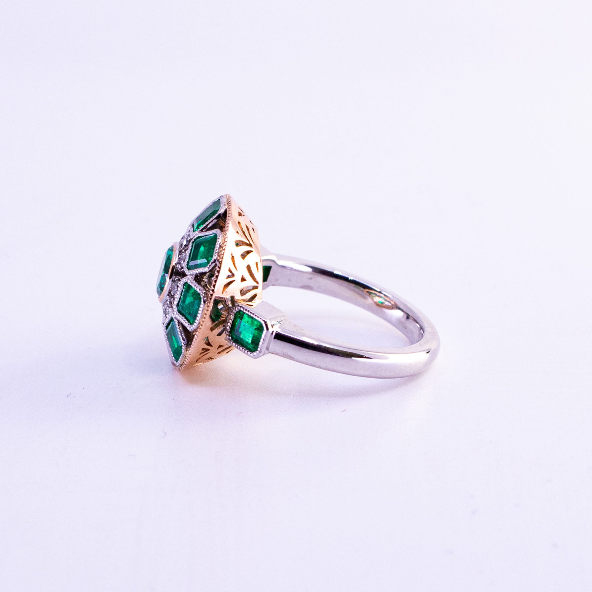 Custom 18ct rose and white gold Art Deco ring featuring central round emerald and halo of square-cut Colombian emeralds with round diamond accents and detailed geometric setting.